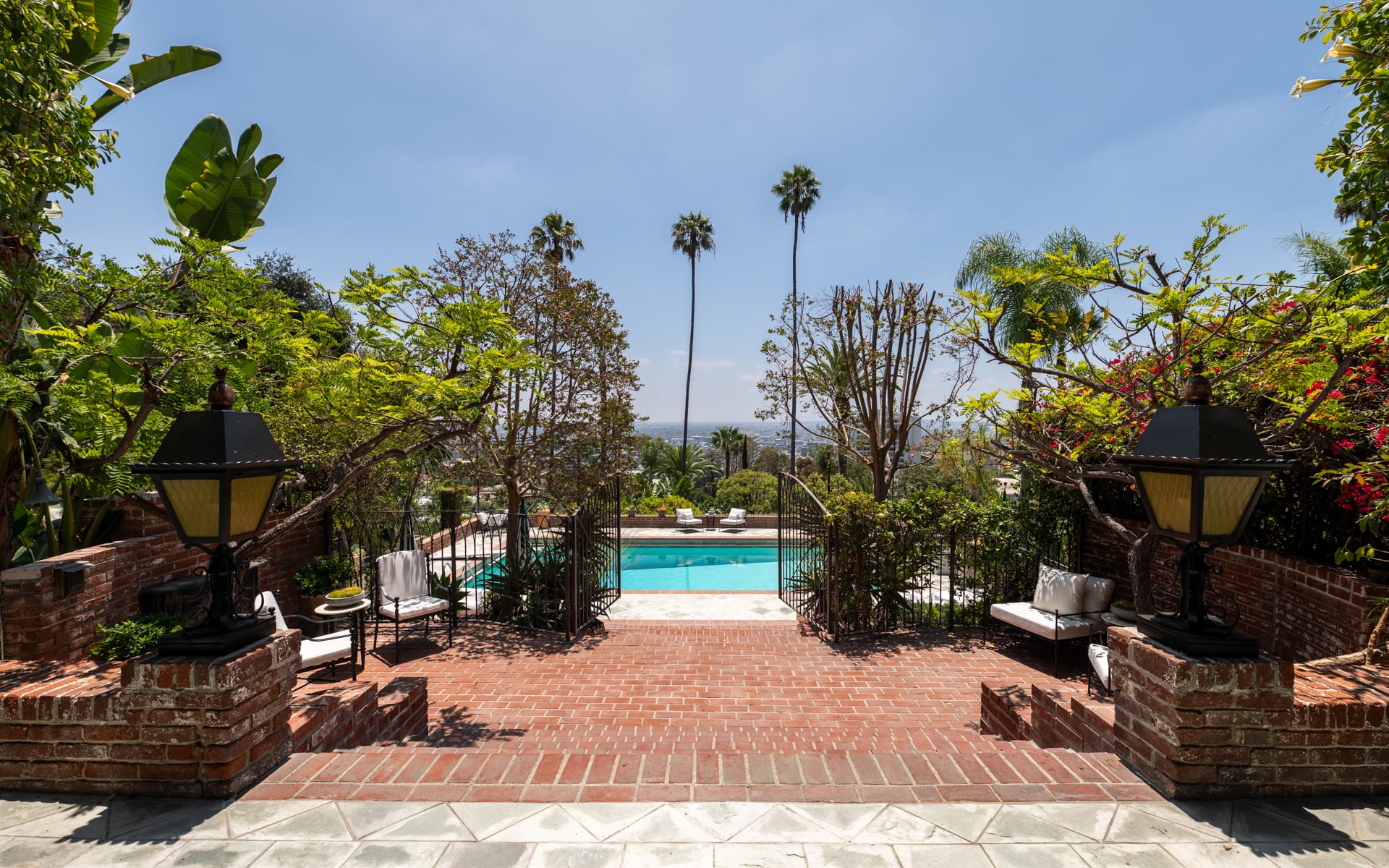 Seating areas are tucked among palm trees and lush plants, while elevated views stretch across the Los Angeles skyline.