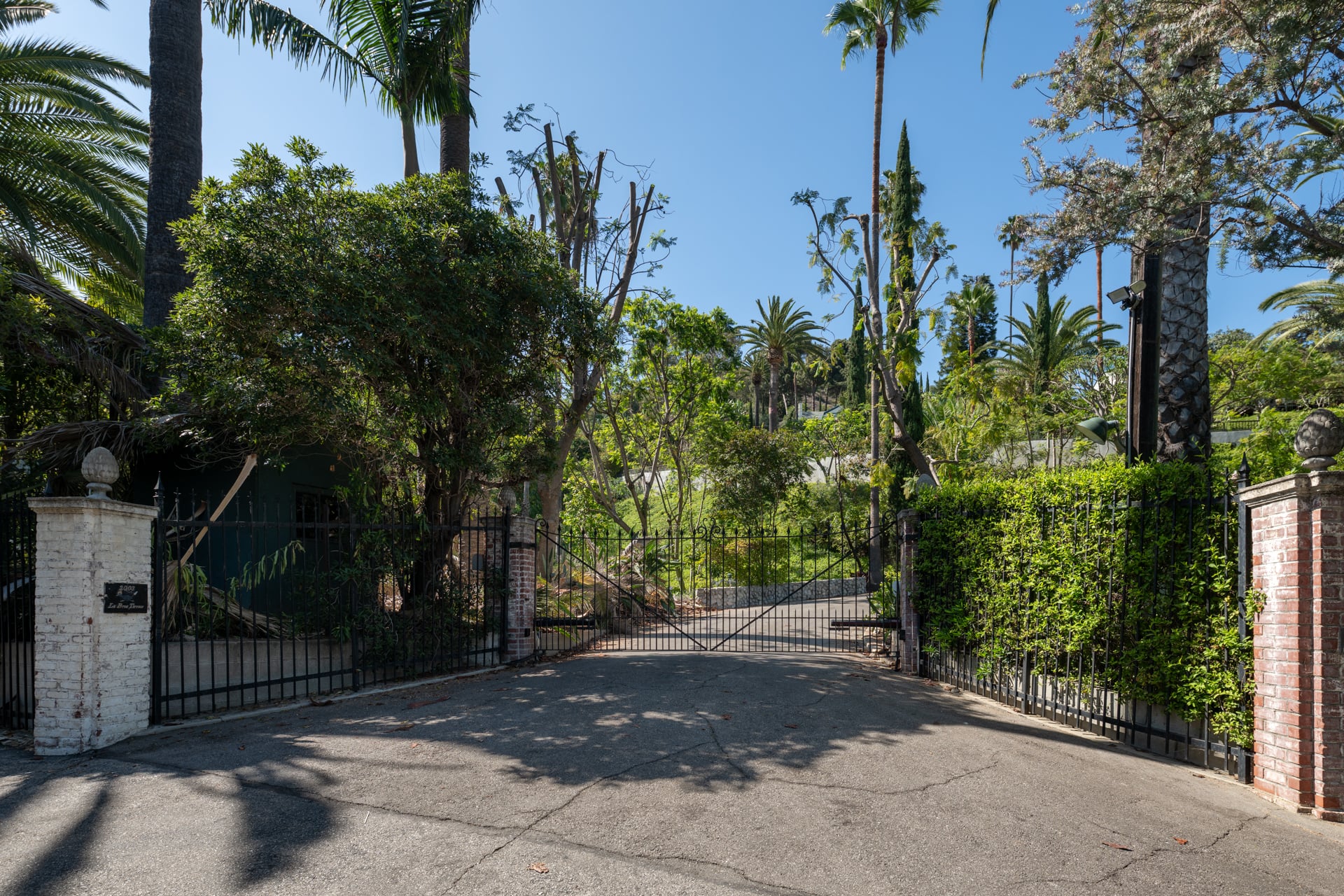 Wrought-iron gates open to a quarter-mile driveway winding uphill through towering trees and dense landscaping.