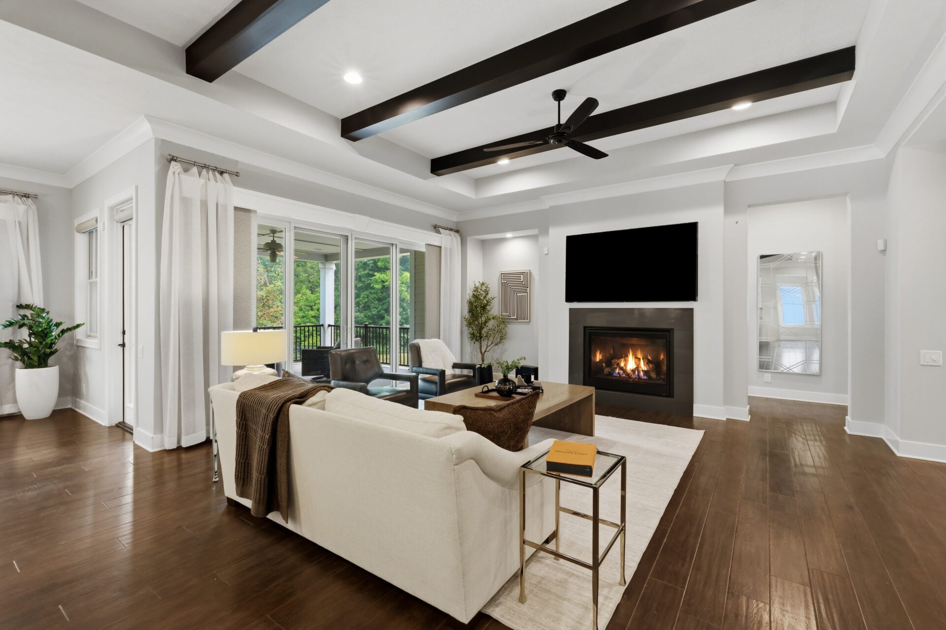 A coffered ceiling with exposed beams defines the seating area, while oversized sliding glass doors fill the room with natural light and open directly onto the covered deck.