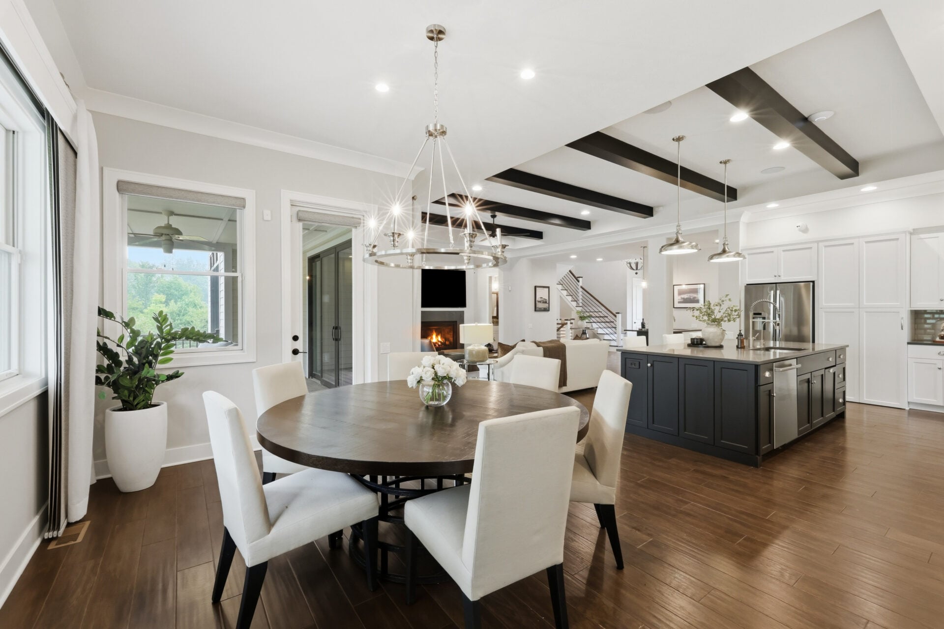 Across from the kitchen, the dining area occupies another of the room's corners beneath a modern chandelier and wrapped in large windows.
