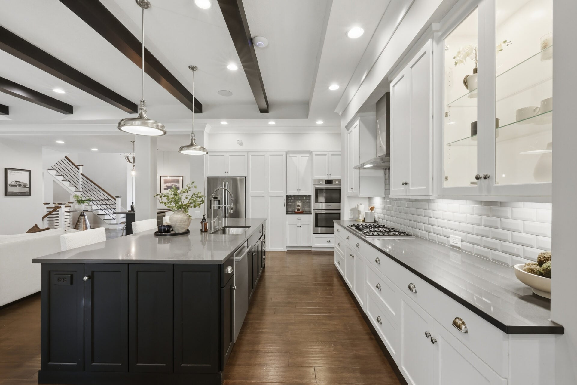 White cabinets wrap the perimeter alongside premium stainless steel appliances, a gas cooktop along the back wall, illuminated display cabinets, and expansive prep counters.