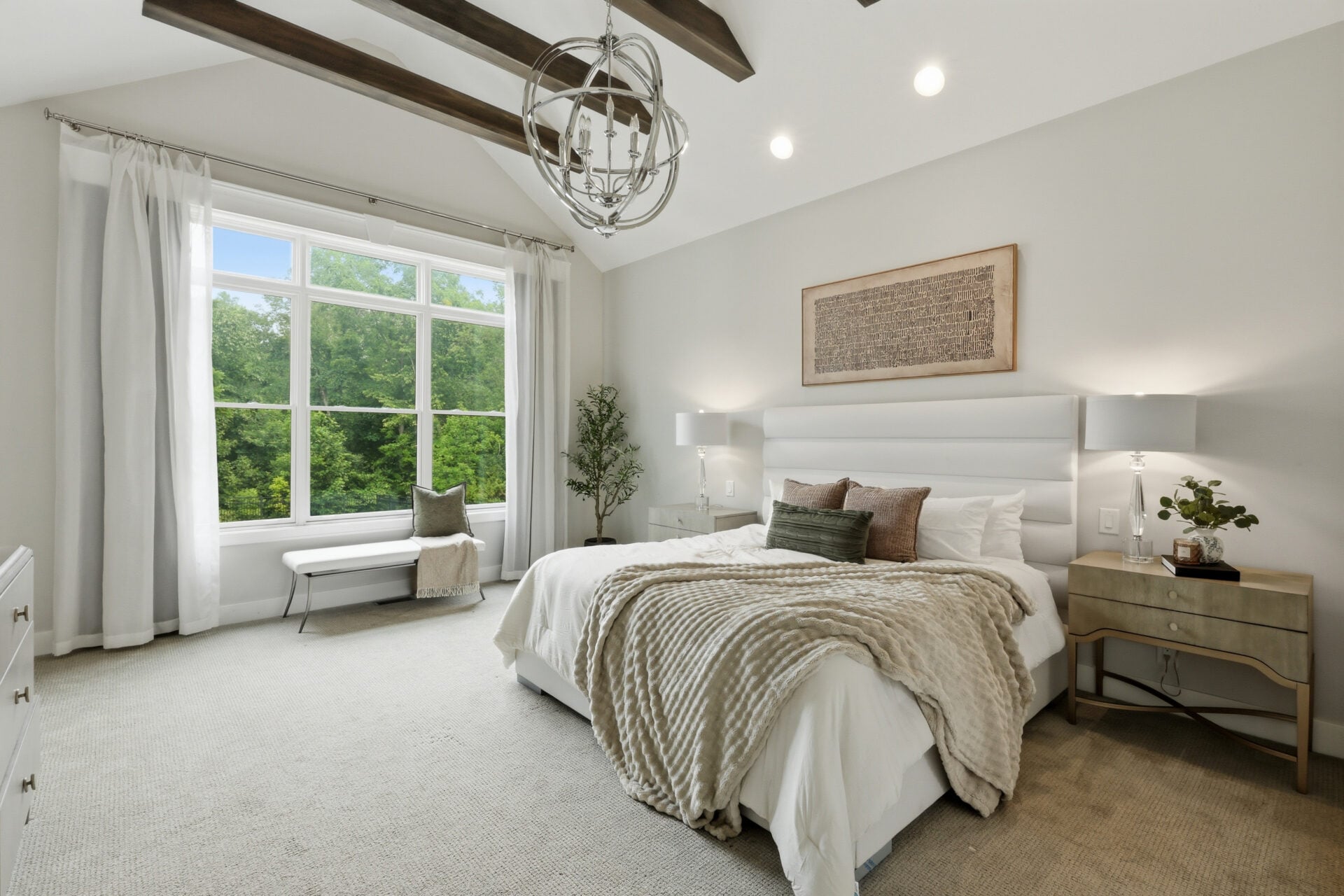 The primary suite occupies its own private corner of the home with a vaulted ceiling accented by exposed wood beams and a large picture window overlooking the surrounding trees.