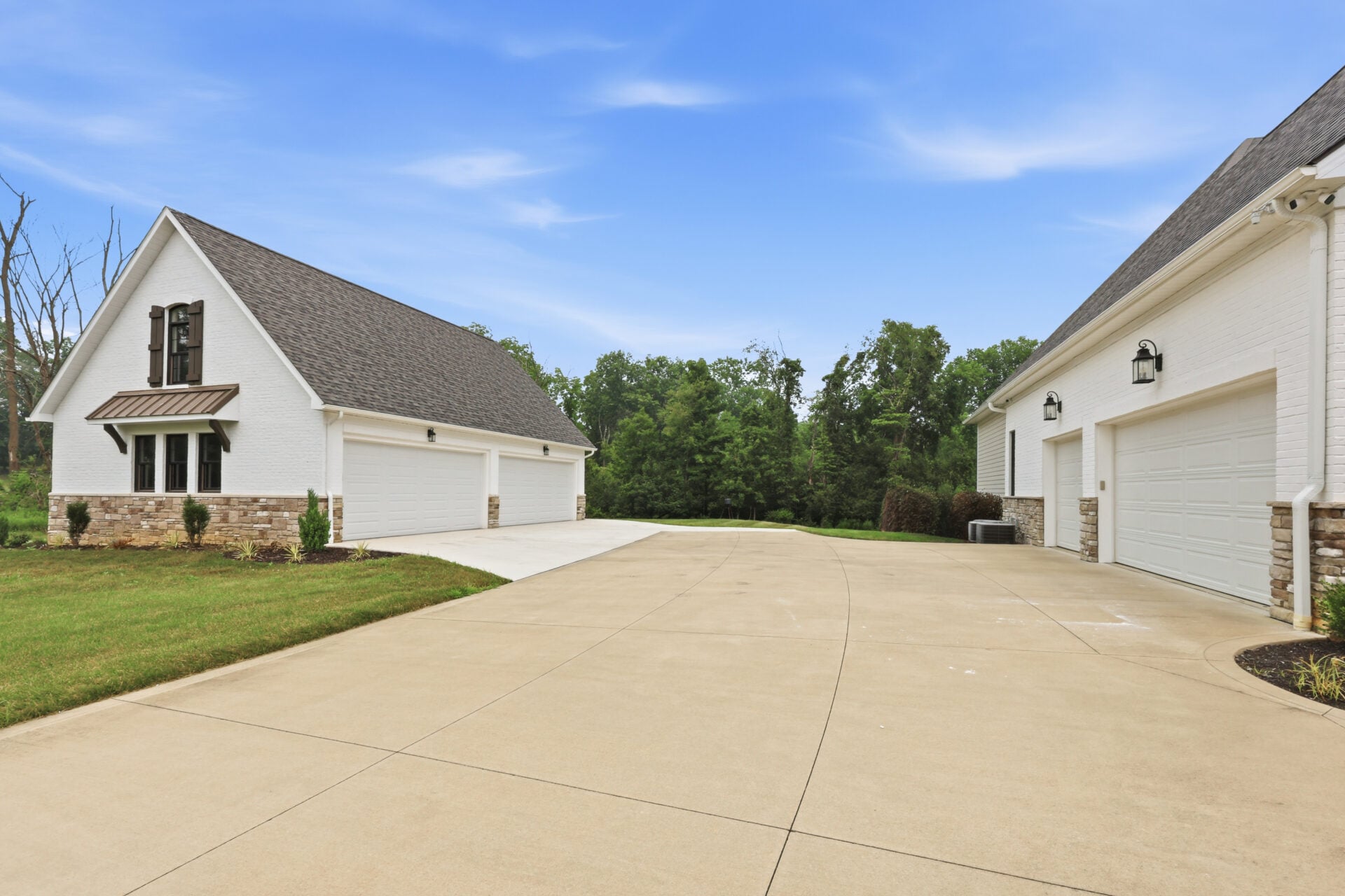 A long concrete driveway opens to an expansive motor court framed by a three-car garage attached to the house on one side and a separate four-car garage on the other. 