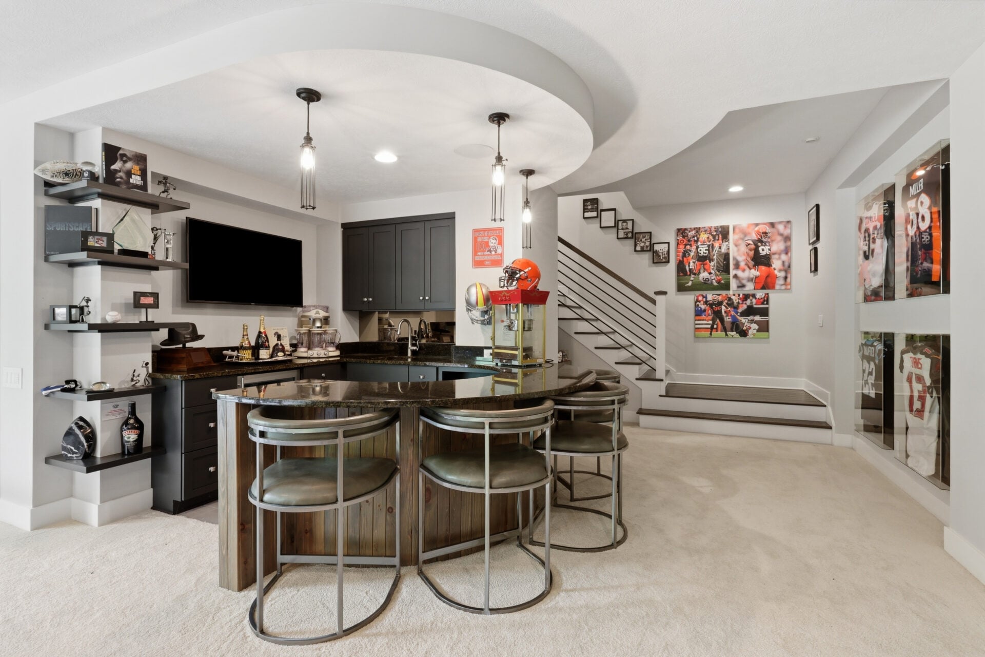 A custom bar where a curved granite countertop is lined with seating and is surrounded by dark cabinetry, open shelving, and a built-in television. 