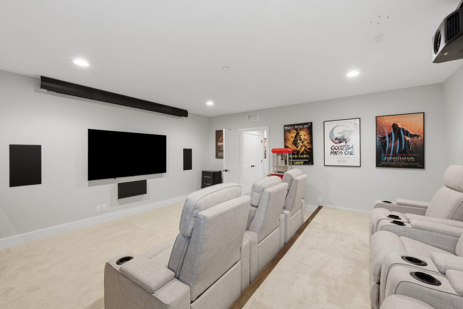 Two rows of reclining theater seats face a large projection screen with built-in surround sound, movie posters, and a classic popcorn machine filling the rest of the room.