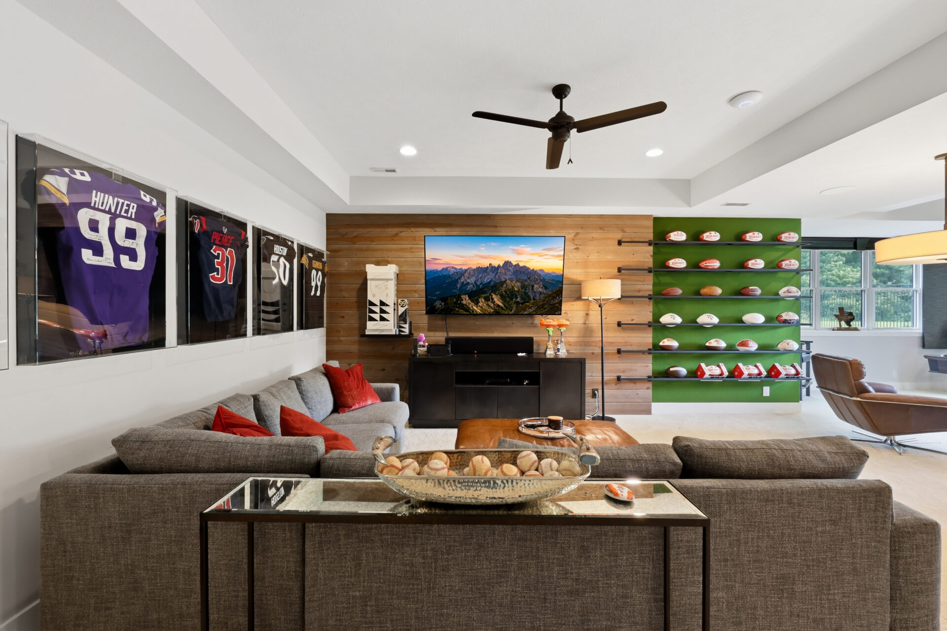 An L-shaped couch offers room to watch games or gather with friends, surrounded by walls that showcase Garrett's collection of signed footballs and framed jerseys from across the NFL.