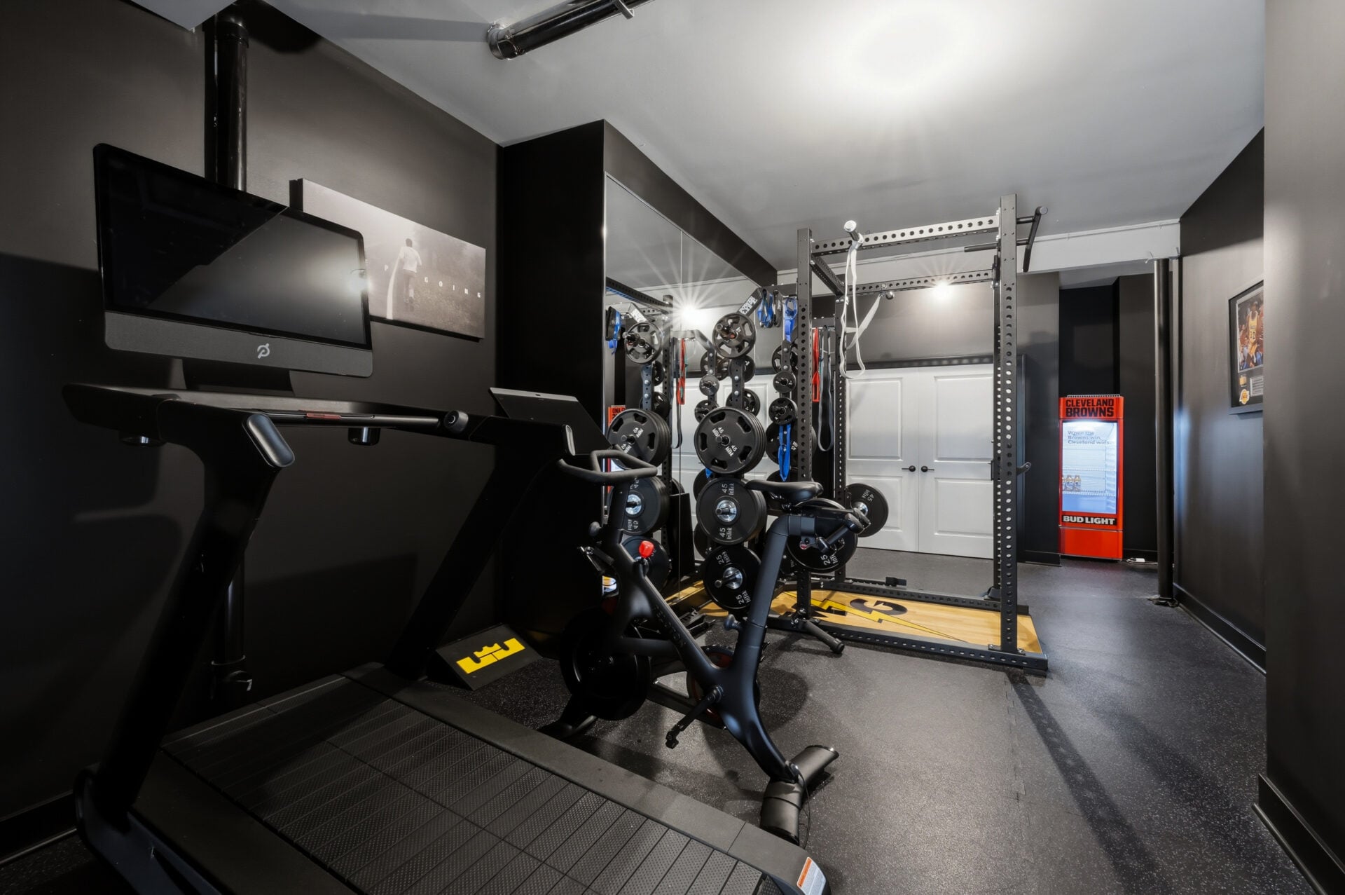 Rubber flooring, a squat rack, cardio equipment, and strength-training machines fill the room.