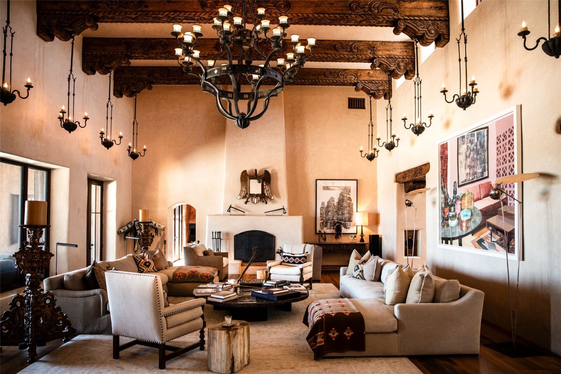 A plaster fireplace sits at one end beneath an antique eagle mirror, while tall windows and glass doors bring in light along the opposite side.