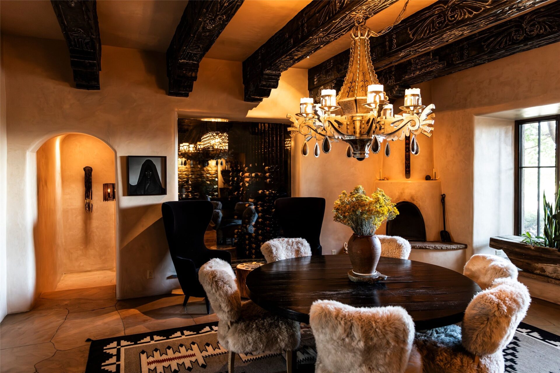 Behind the round table, a dark glass opening reveals the wine cellar, where bottles are stacked across floor-to-ceiling racks.