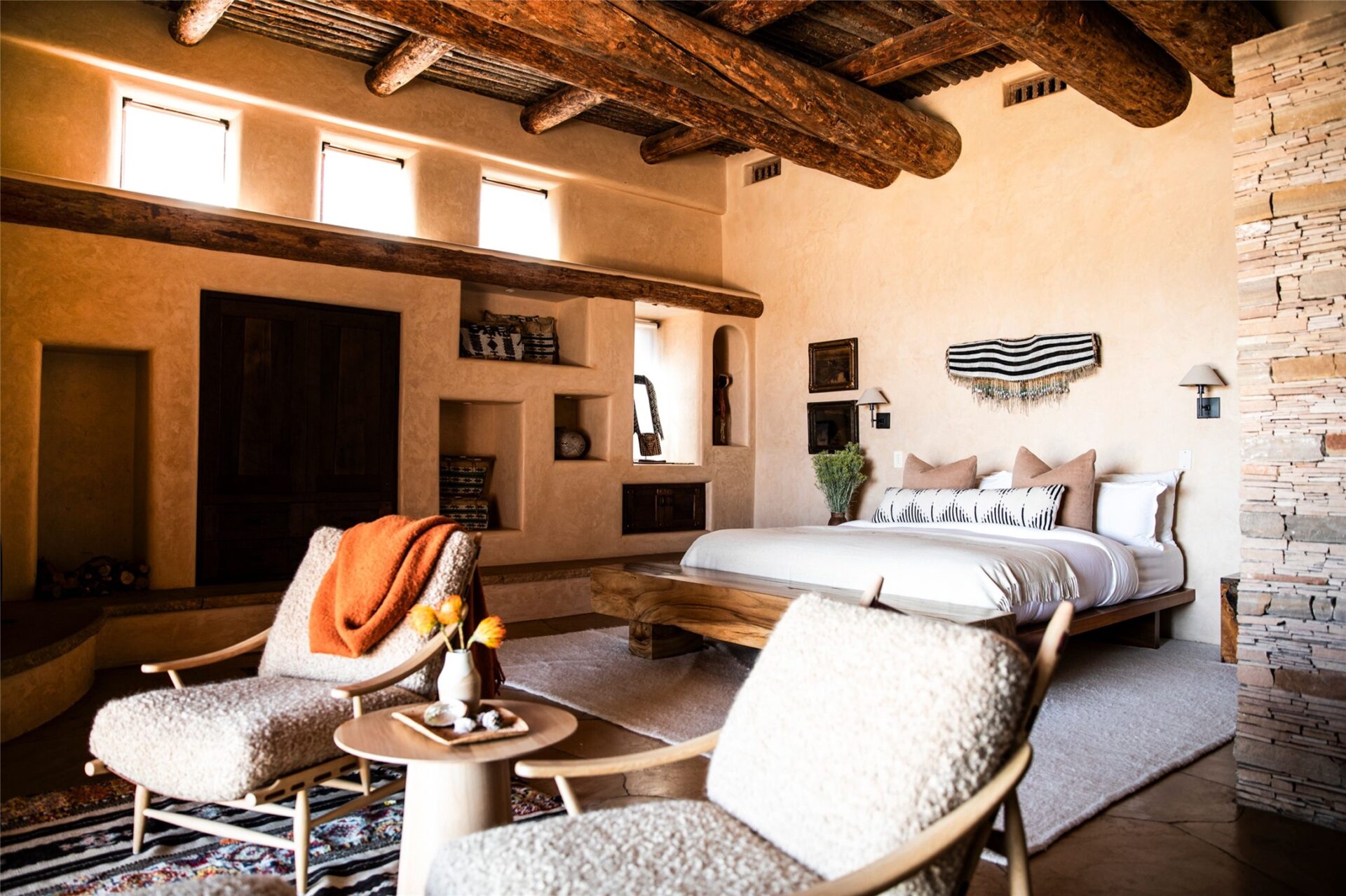 A low timber bed is set beside a stacked-stone wall, while built-in niches and dark wood doors are worked directly into the plaster walls.