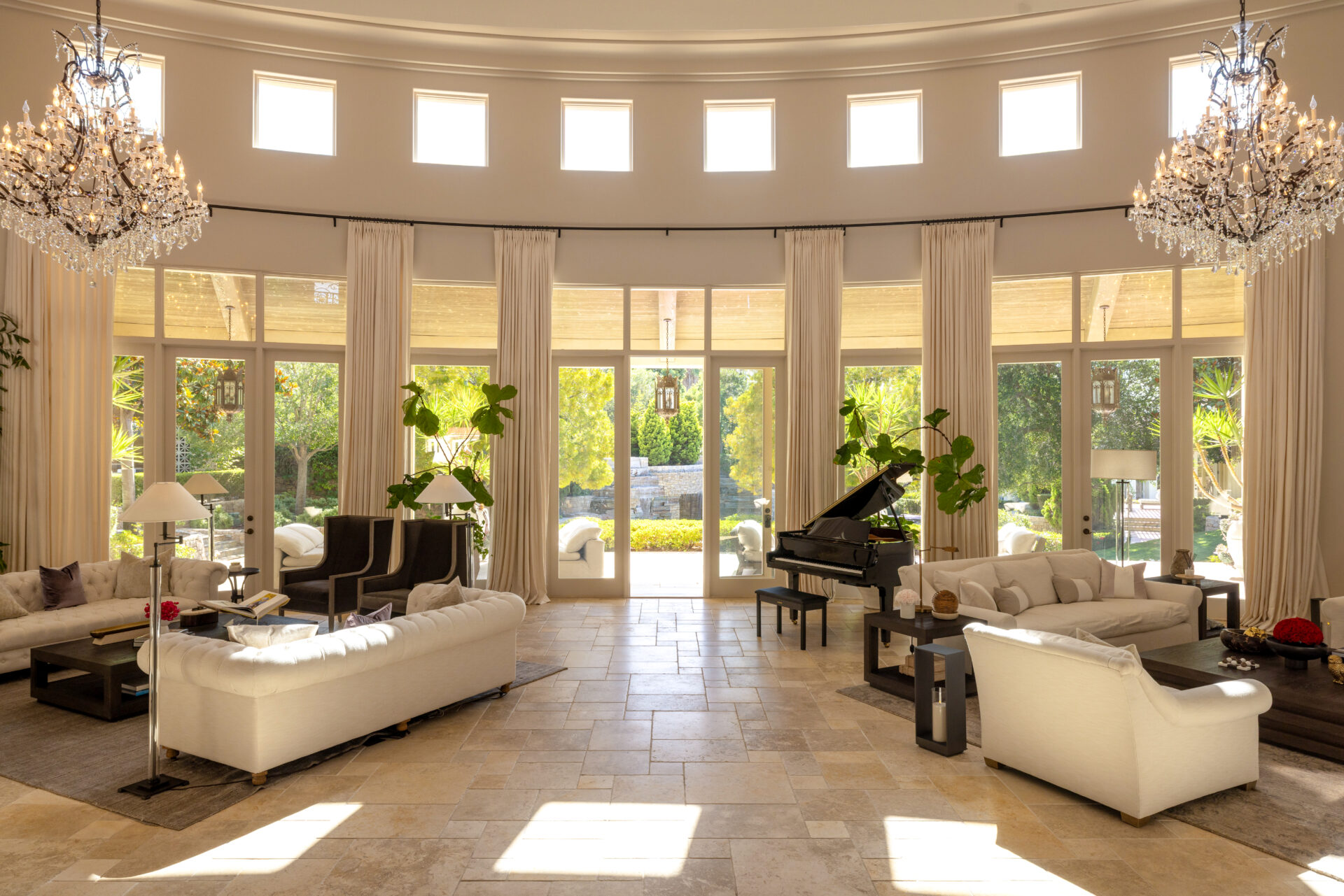 Two seating areas are arranged across the limestone floor, with white tufted sofas and dark wood tables leaving a clear path through the center toward the Loggia.