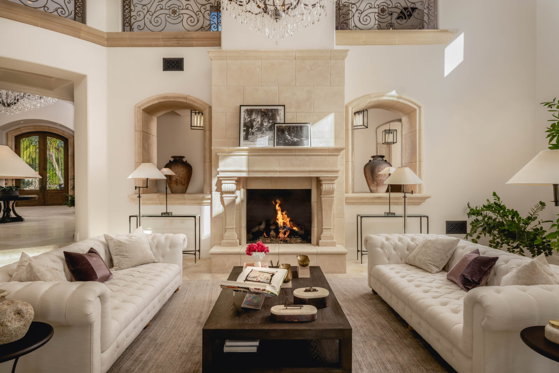 A carved stone fireplace rises beneath the upper-level gallery, with arched openings on either side connecting the room back to the entry hall.