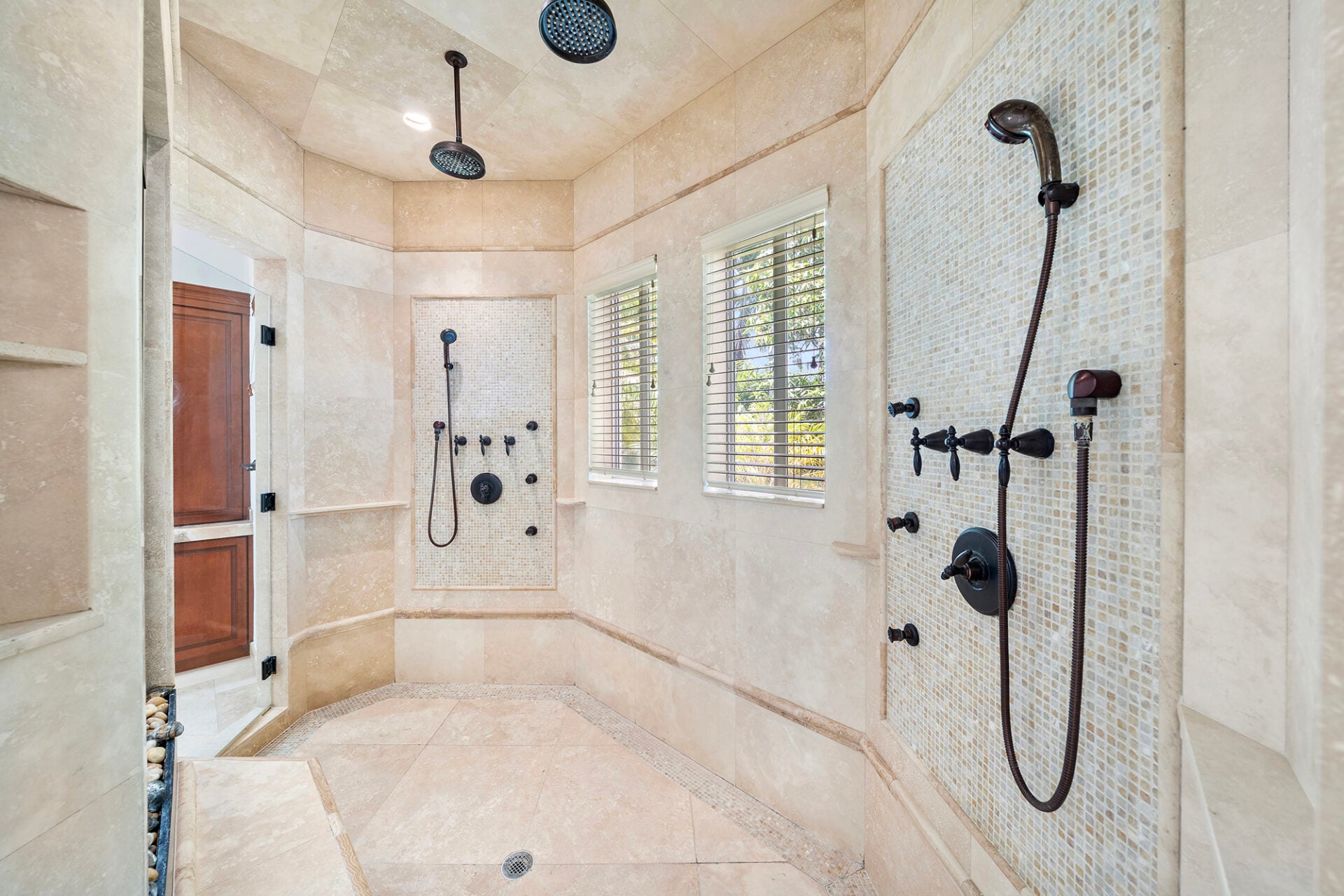 Oversized walk-in shower finished in floor-to-ceiling natural stone with two sets of rainfall showerheads, body sprays, and handheld fixtures.