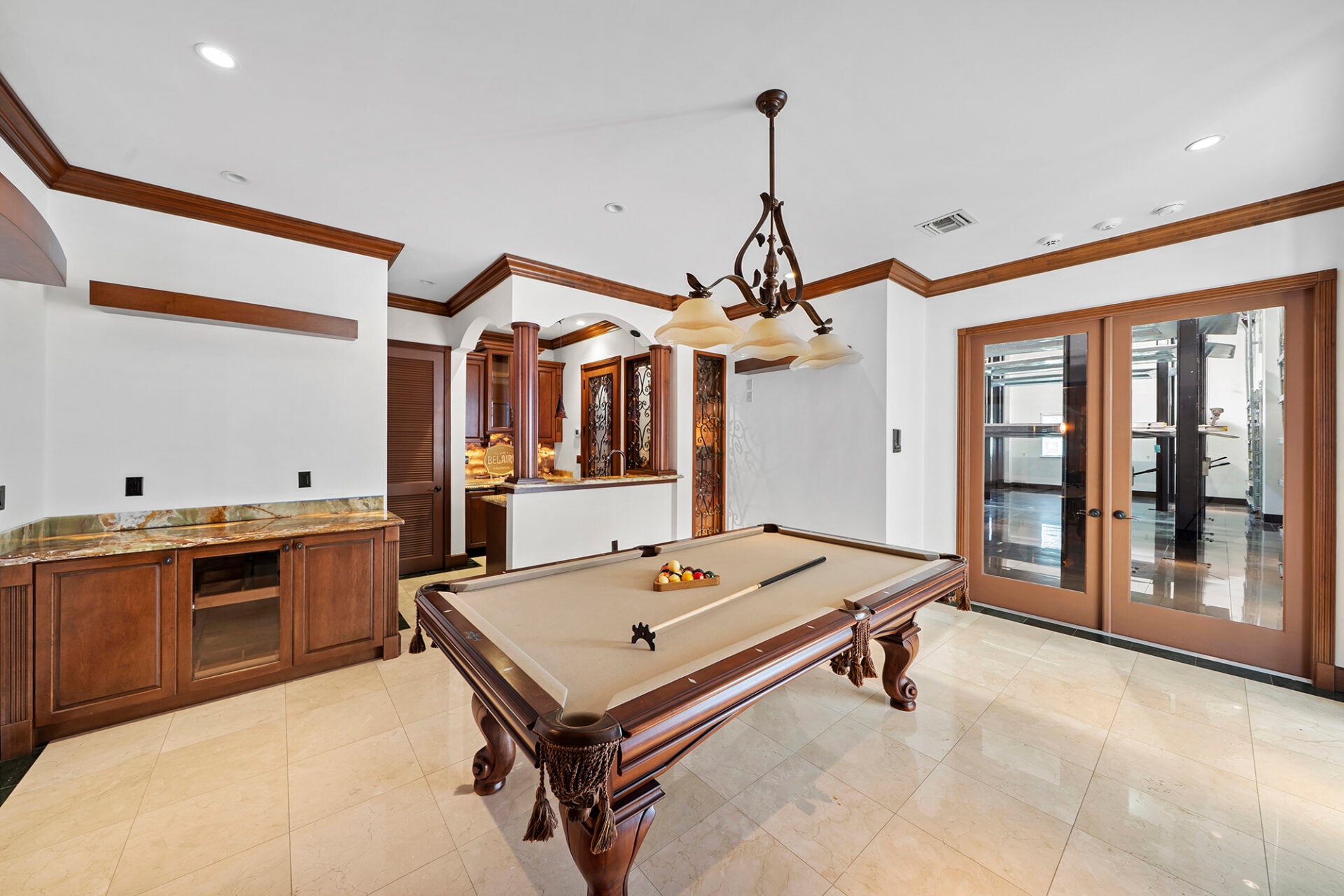 The billiards lounge, centered around a full-size pool table beneath a classic three-light fixture, with custom wood cabinetry providing additional storage along one wall. 