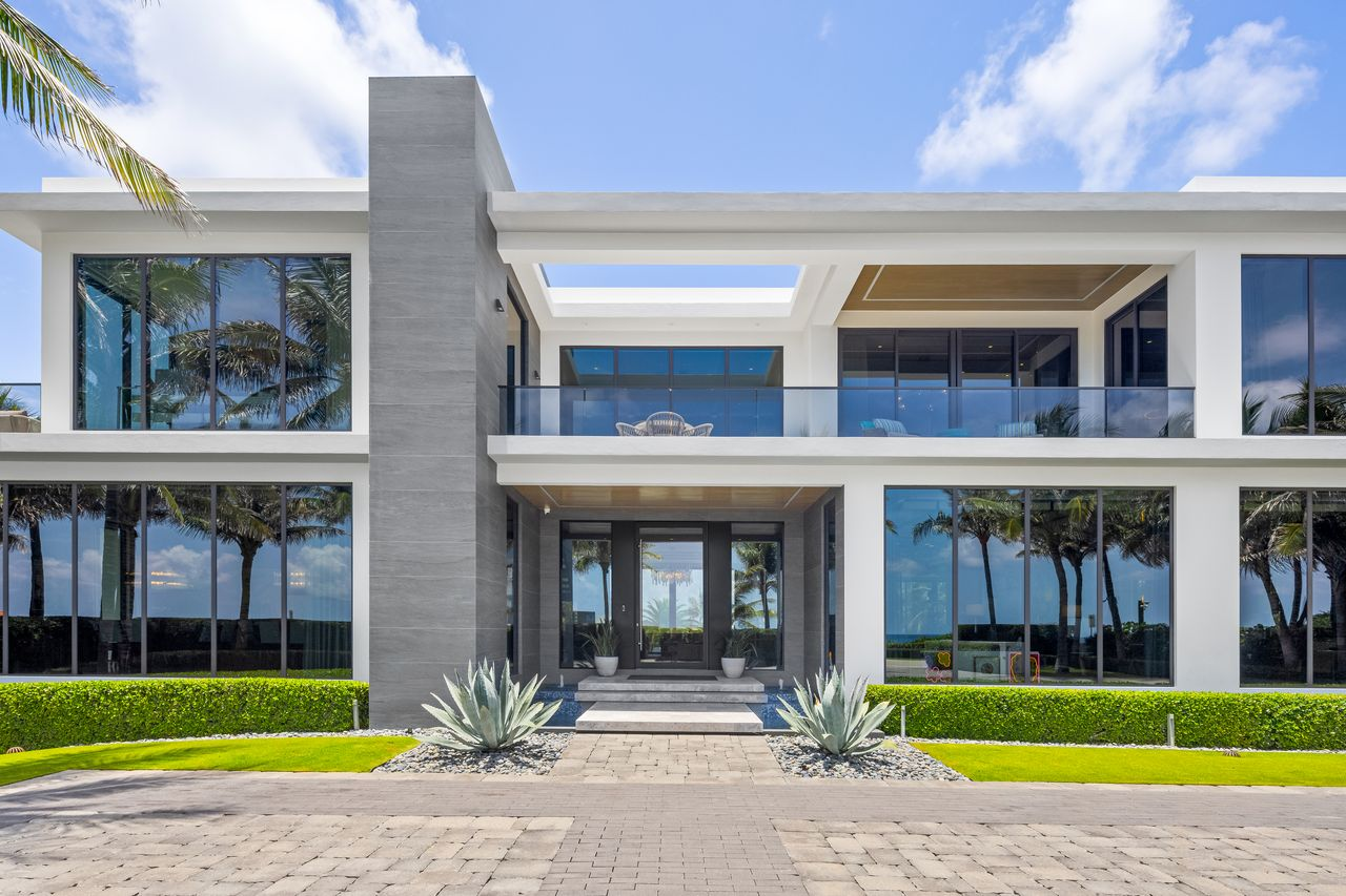Towering walls of glass wrap around both levels, while glass-railed balconies and deep roof overhangs reinforce the home's modern design.