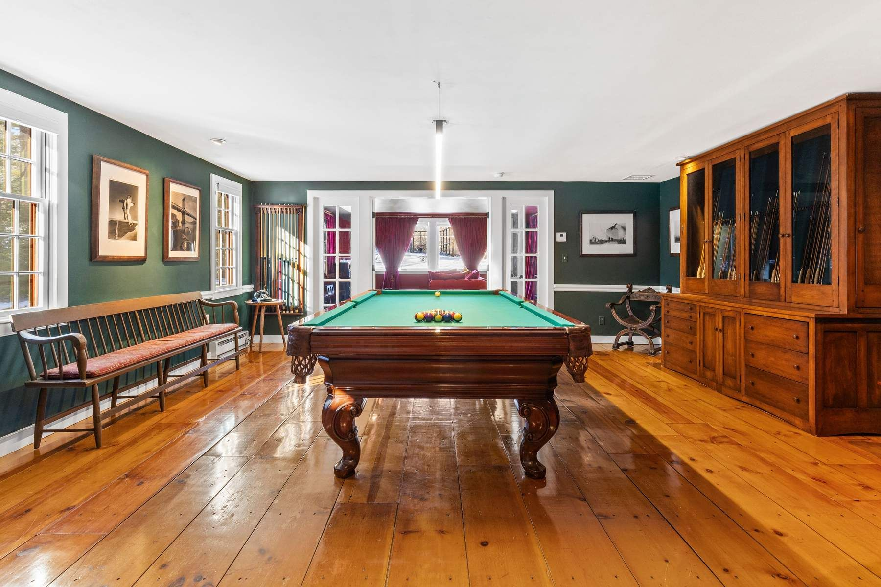 Wide-plank wood floors, deep green walls, and built-in cabinetry give the room a classic look, while French doors open into the media lounge.