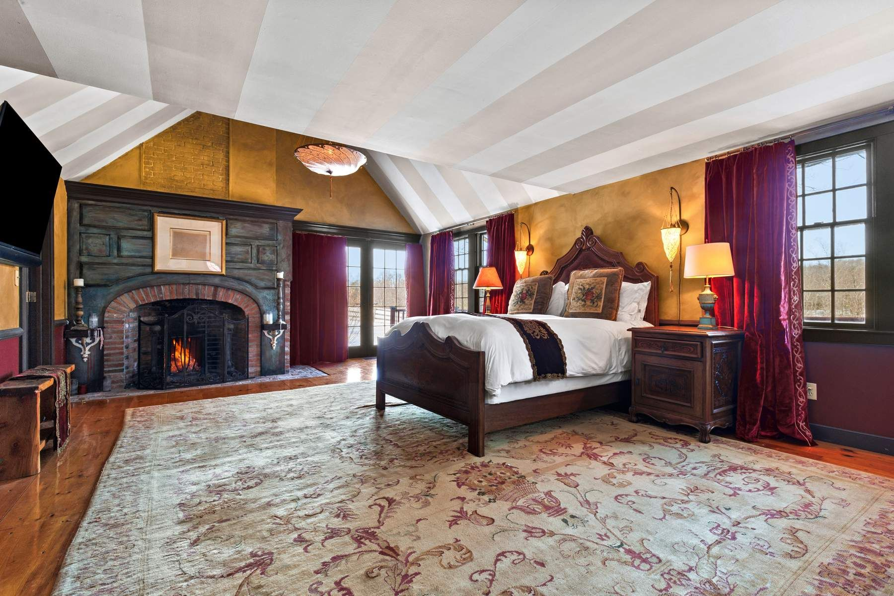 A spacious bedroom centered around a carved wood bed facing a brick fireplace with a dark paneled mantel.