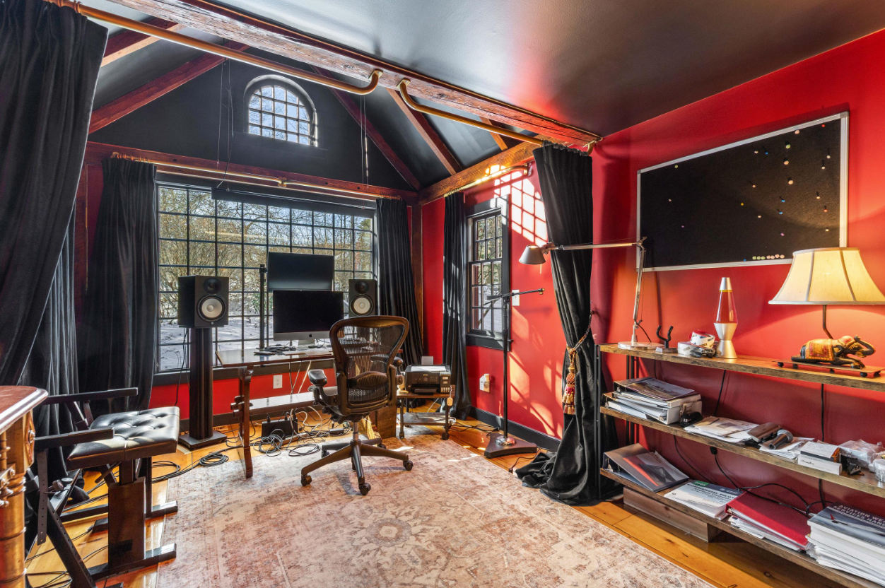 The studio features dramatic red walls, exposed timber framing, and oversized gridded windows that fill the space with natural light.