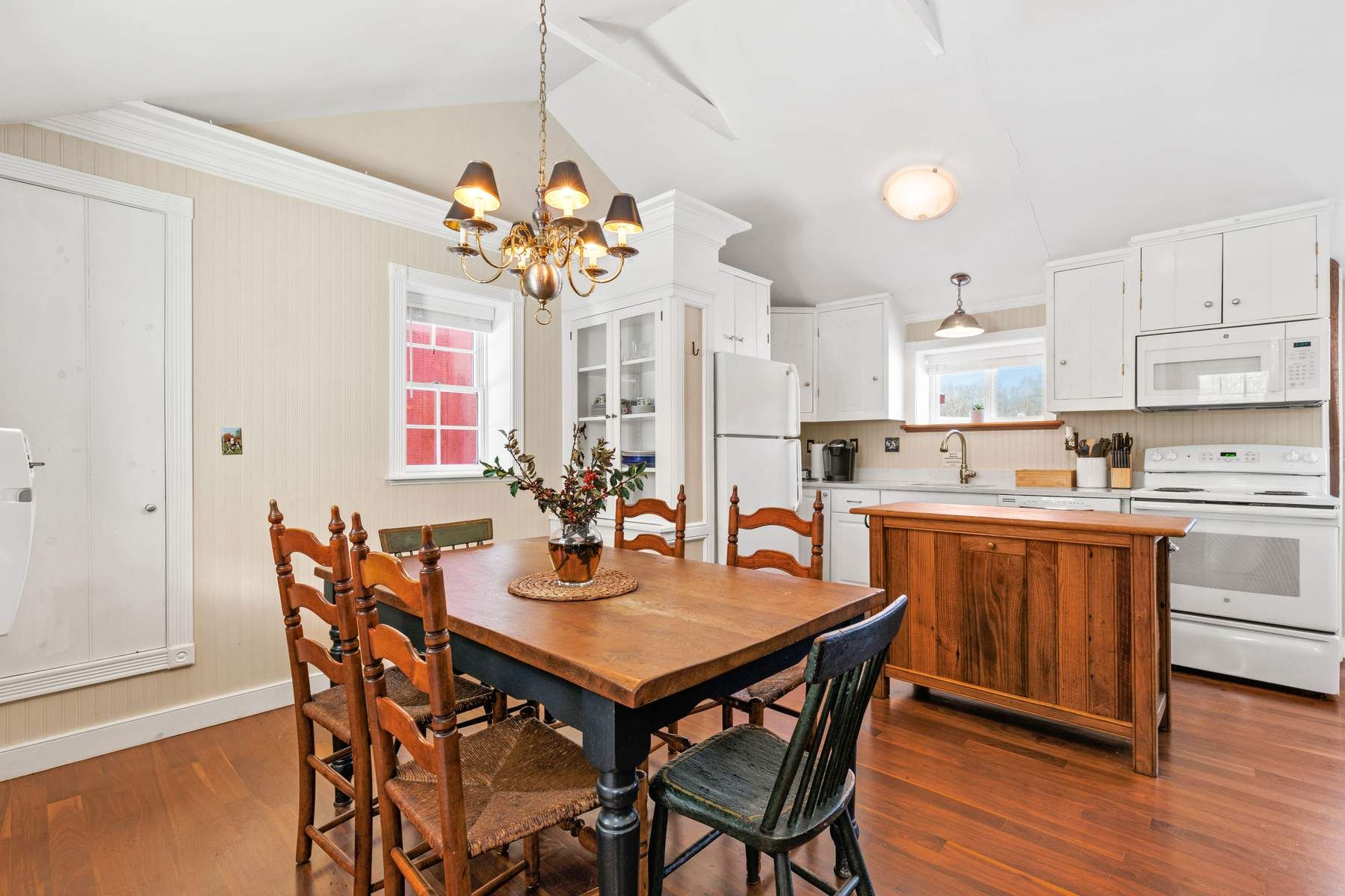 Dining space and kitchen beneath a vaulted ceiling with exposed beams and a central chandelier.