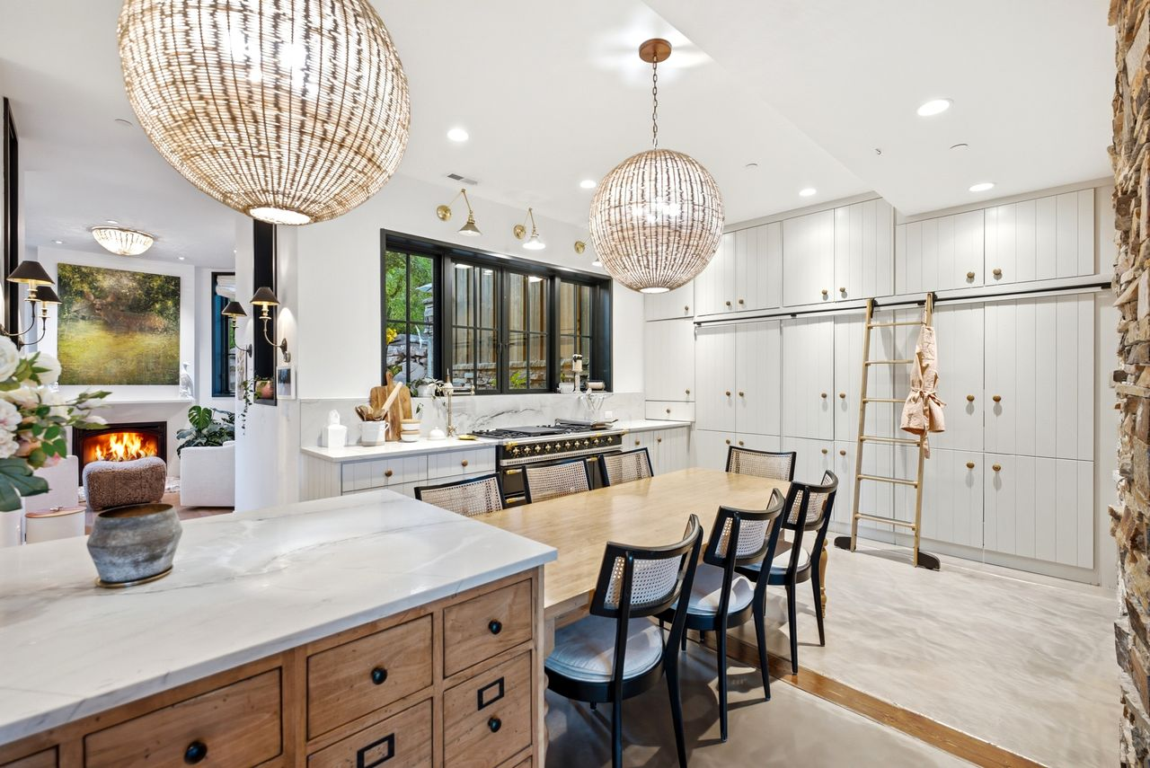 A large marble-topped island that expands into a built-in dining table beneath oversized woven pendant lights.