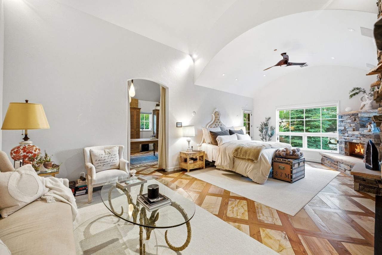 The bedroom opens with soaring vaulted ceilings and a stone fireplace in the corner of the room.