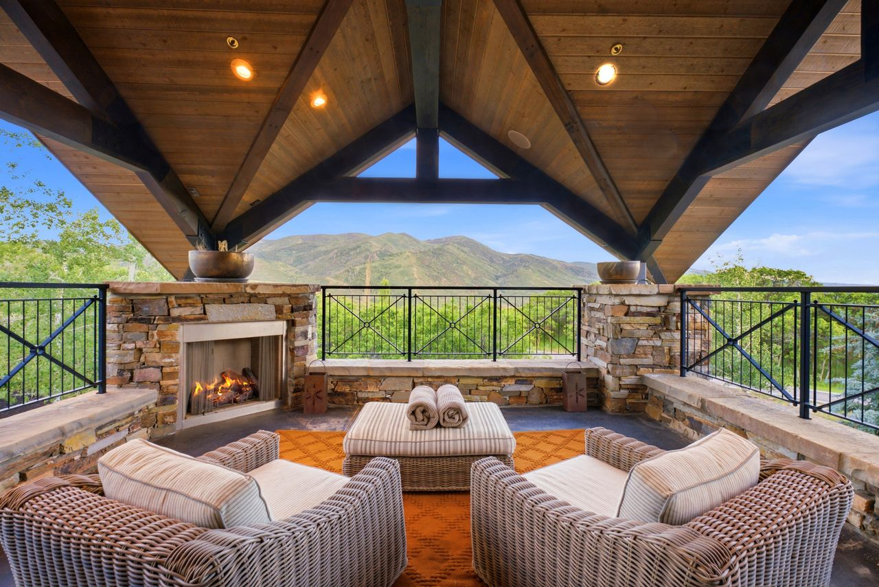 Outdoor terrace set beneath exposed timber trusses with a stone fireplace to create a cozy lounge.
