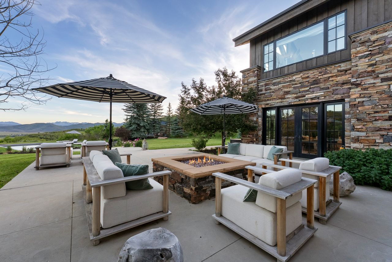 A firepit lounge is arranged with deep cushioned seating around a square gas fire feature.