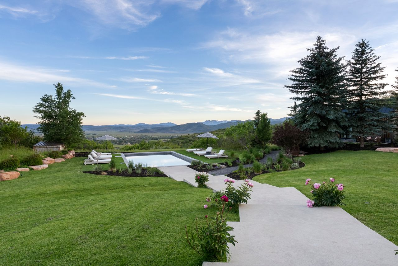Wide concrete walkways lead from the upper patio through manicured lawns to a heated rectangular pool.