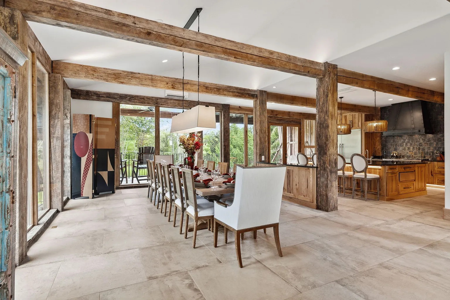 Exposed timber beams continue overhead while a long dining table sits beneath a suspended linear light fixture.