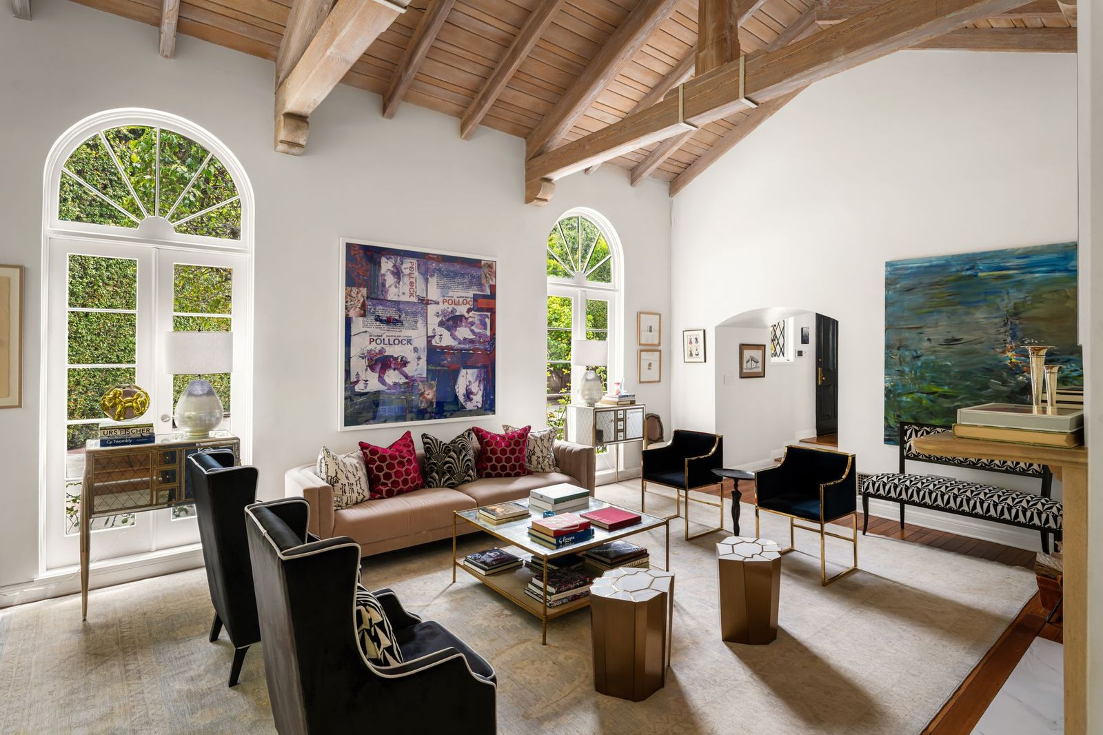 Living room with a vaulted wood-beamed ceiling, crisp white walls, and tall arched windows that flood the space with natural light. 