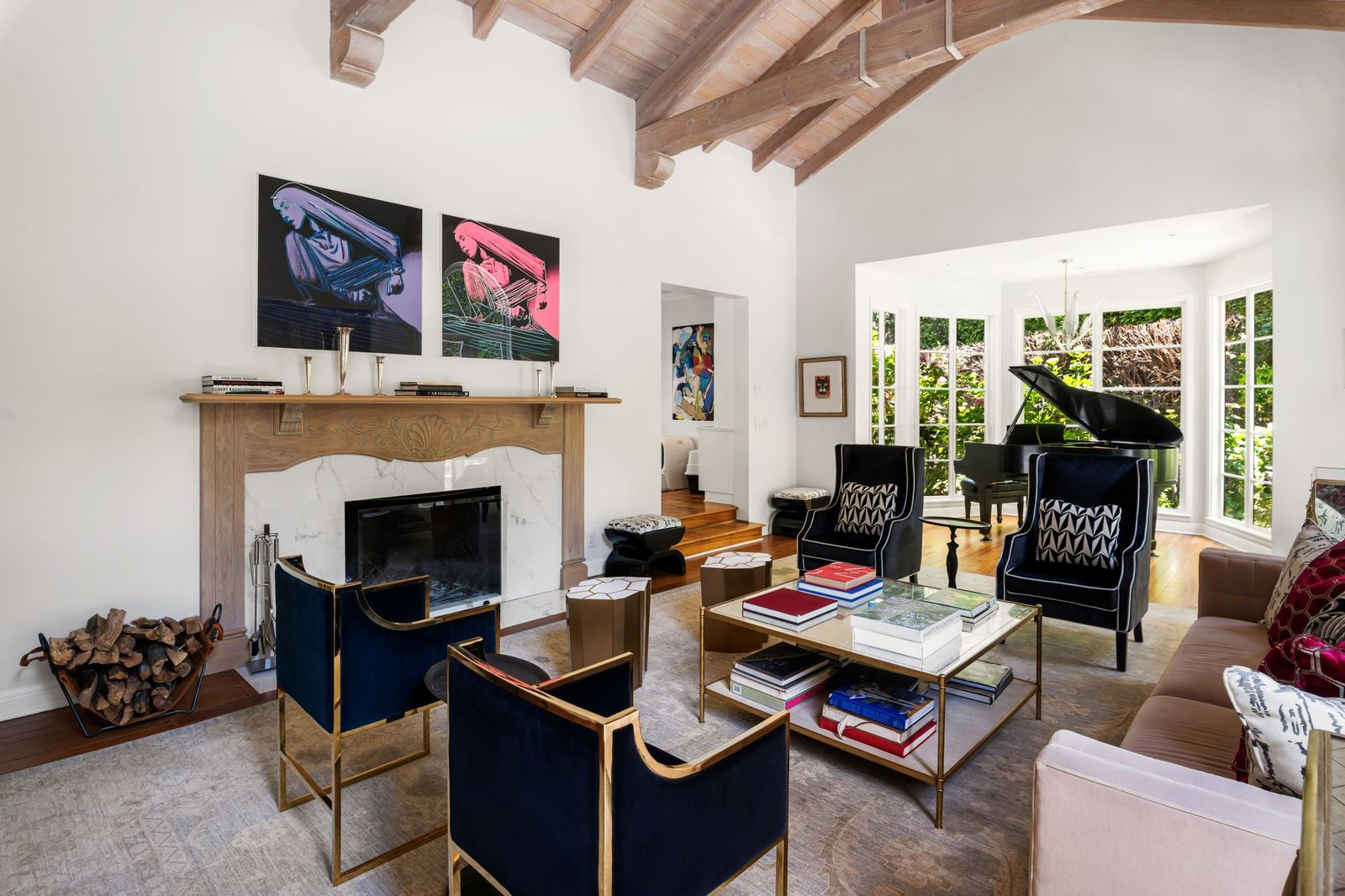 A stone fireplace with a carved wood mantel sits across from the seating area with velvet accent chairs, brass-framed tables, and plush seating.