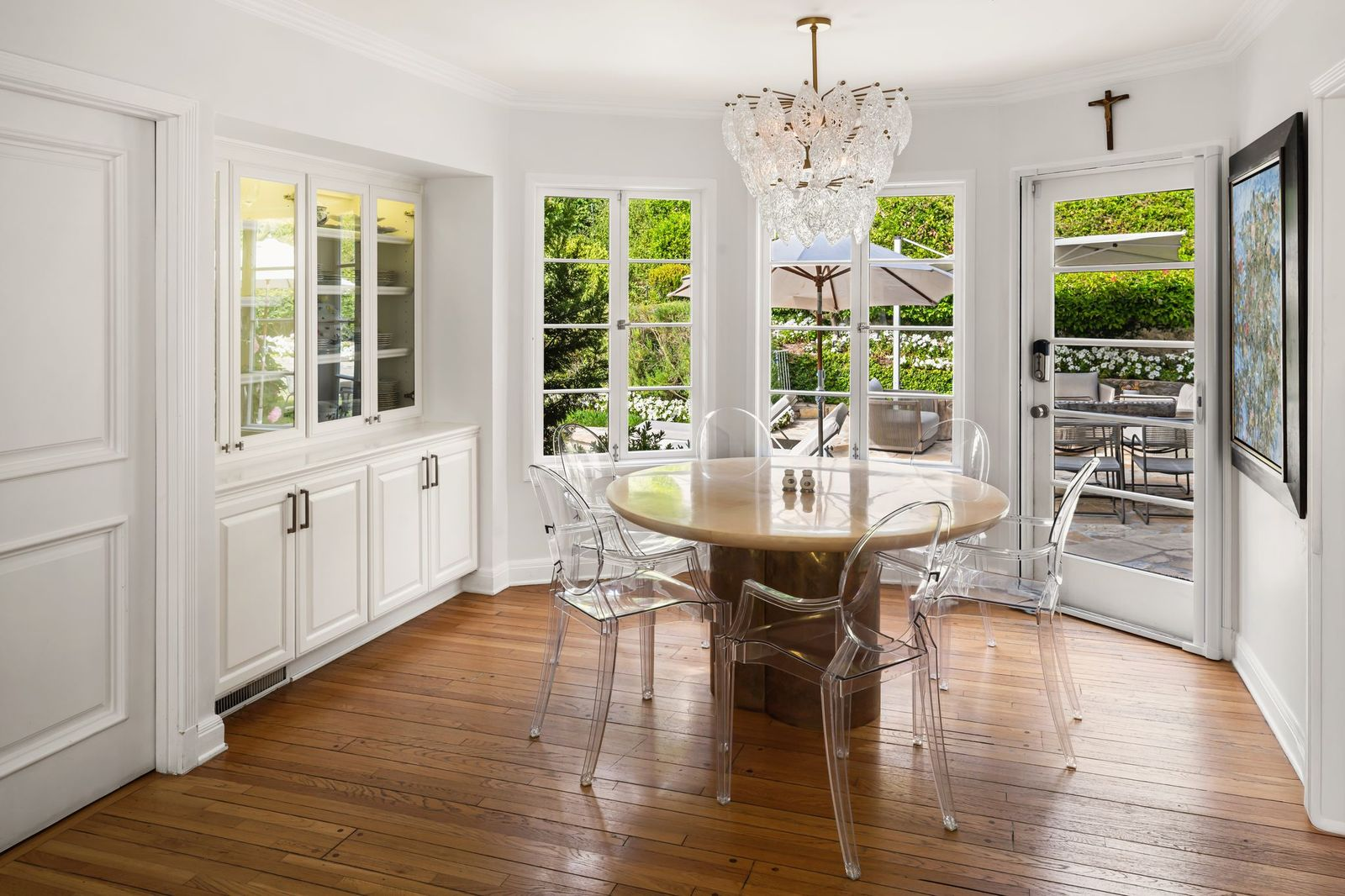 A round pedestal table sits beneath a sculptural glass chandelier, surrounded by transparent acrylic chairs that keep the room feeling light and open. 