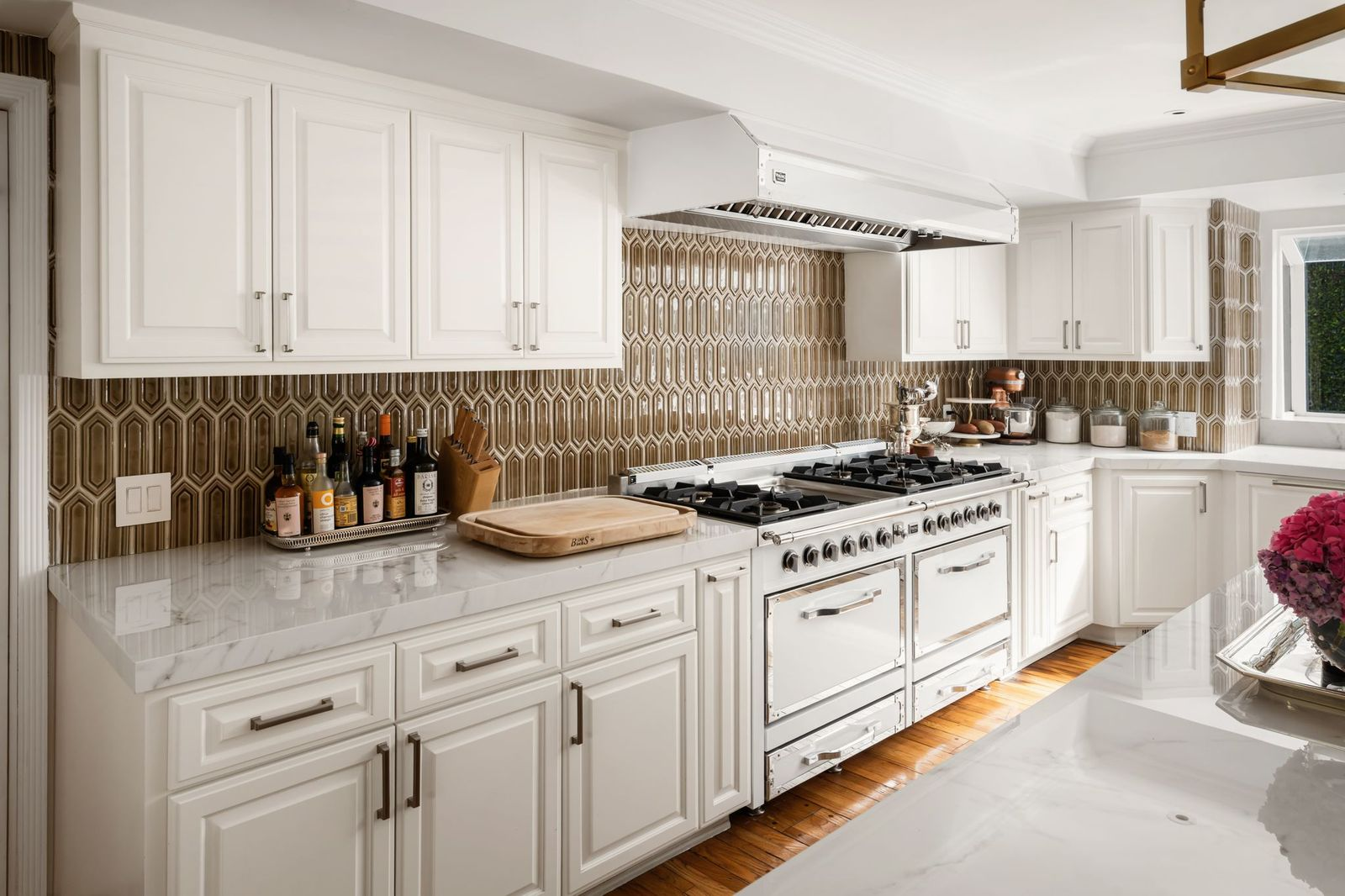 White custom cabinetry is paired with marble countertops and a geometric tile backsplash similar to the one in the bar, but in a light brown.