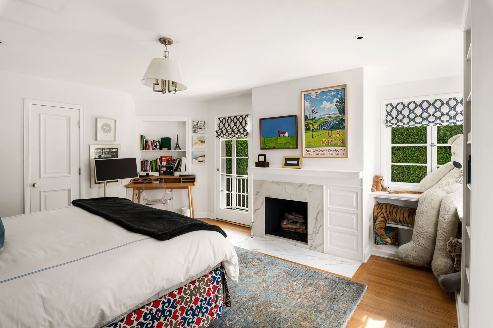 A guest bedroom features a marble fireplace with built-in cabinetry, a dedicated desk nook, and a door that opens onto a covered balcony.