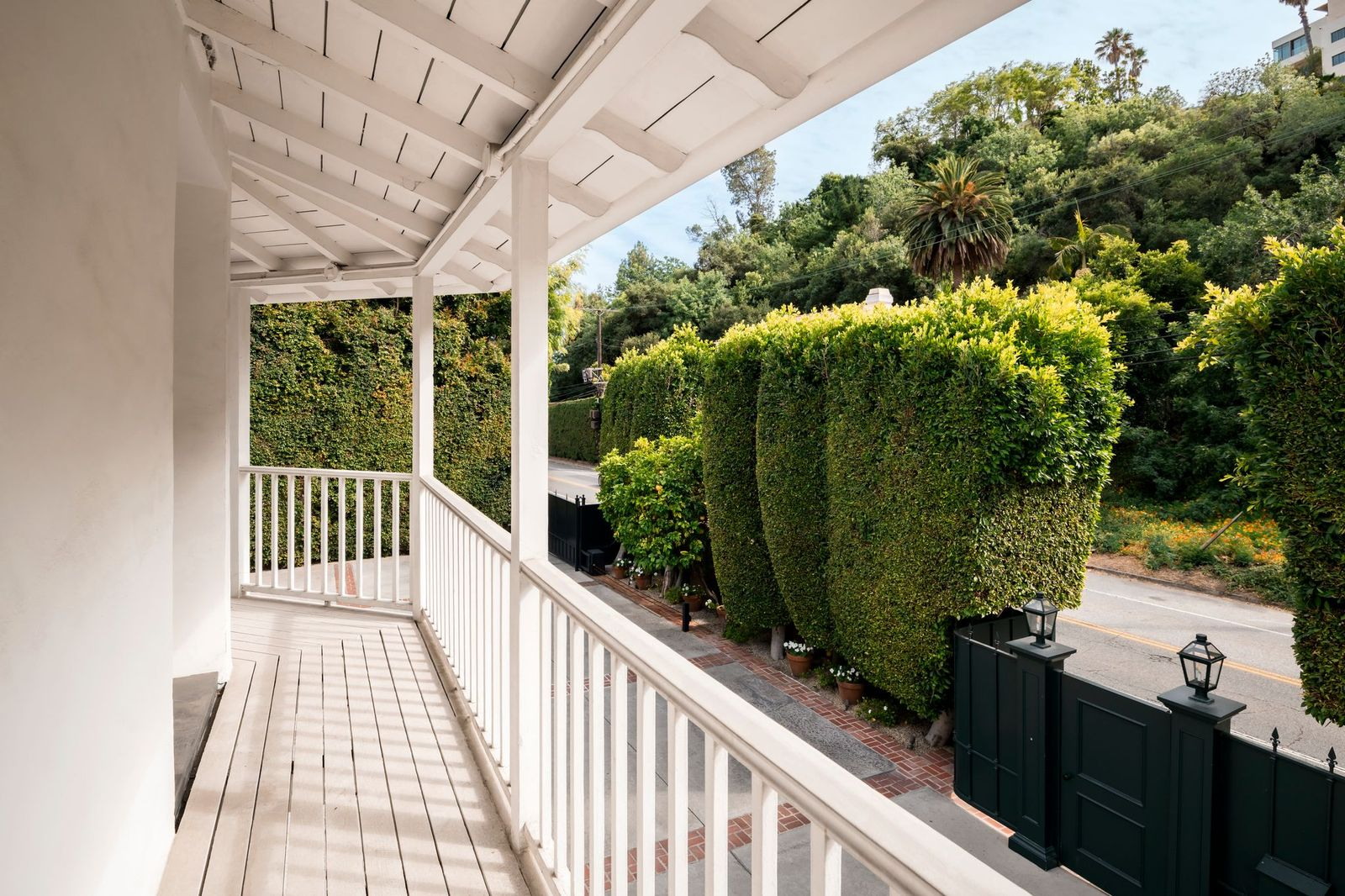 The long veranda overlooks the gated front grounds and surrounding greenery, extending the bedroom and upper level to the outdoors.