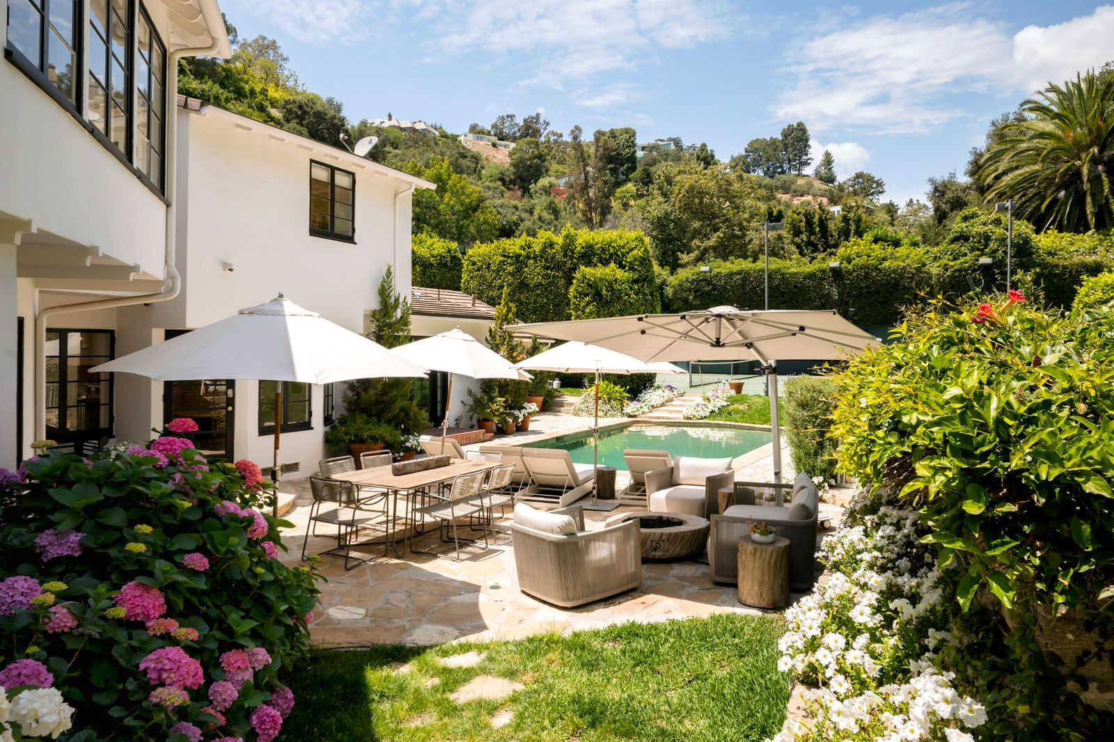 A broad stone patio serves as the main entertaining area with a dining table and a lounge area placed around a circular fire pit.