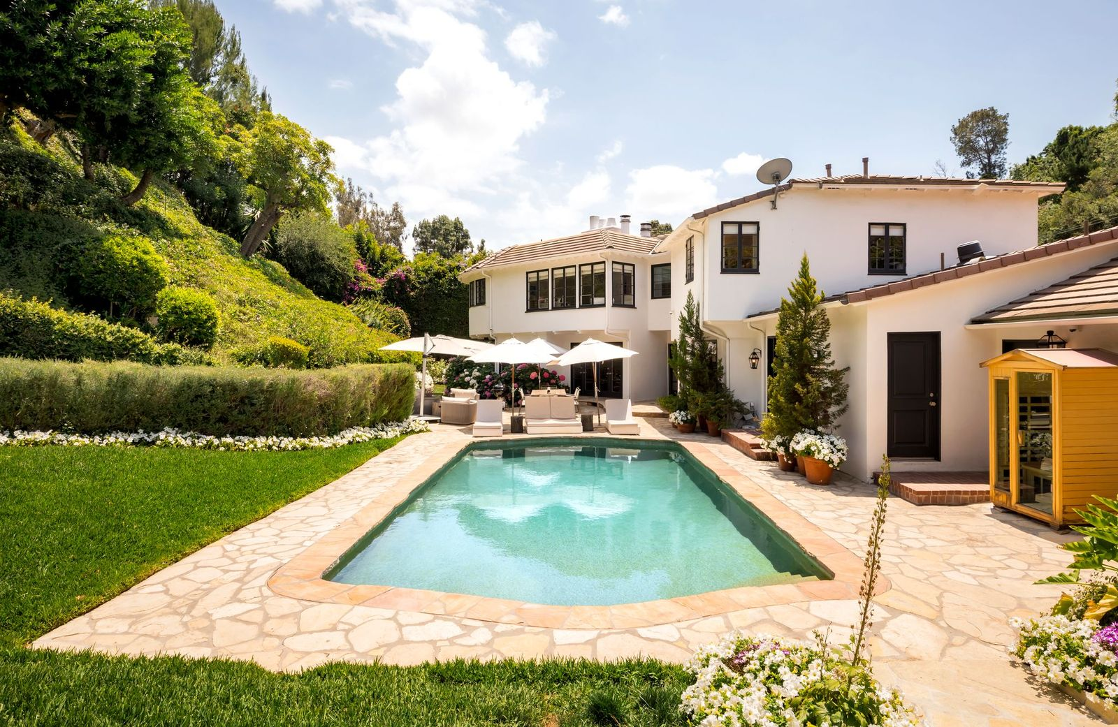A row of lounge chairs separates the entertaining patio from the swimming pool, which is framed by stone decking and sits only steps away from a sauna.