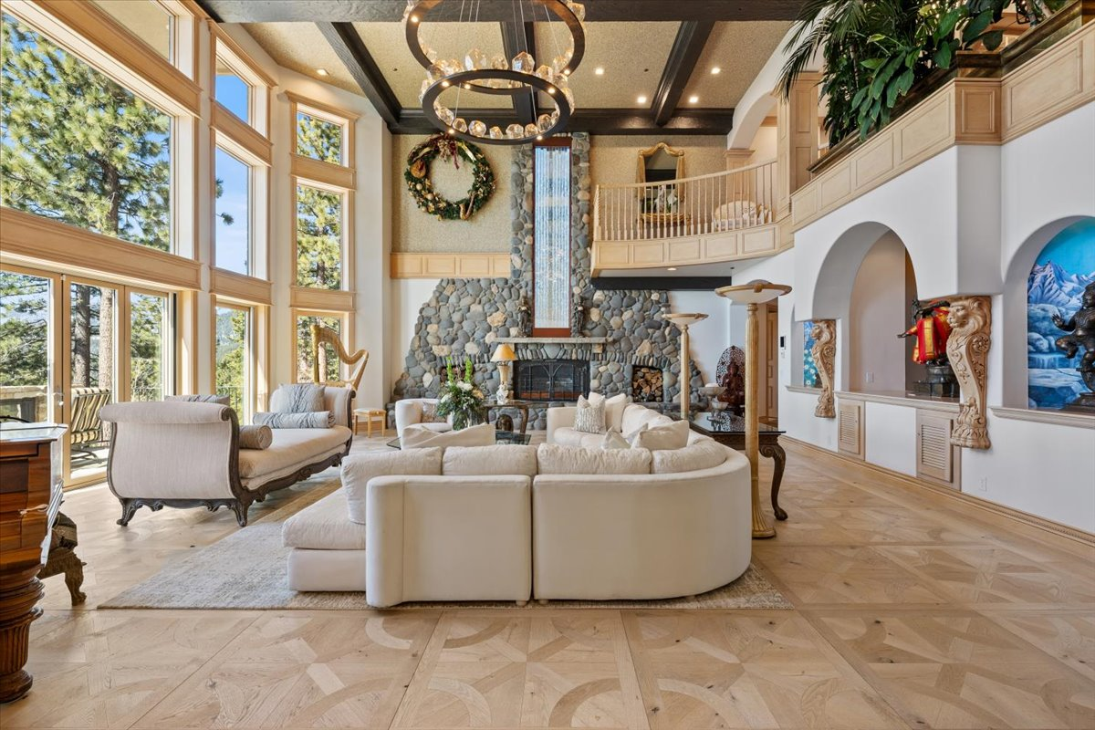 A soaring two-story river rock fireplace with a cobblestone hearth and native stone mantel sits on the opposite wall, complemented by a dramatic waterfall feature that cascades from the upper level. 