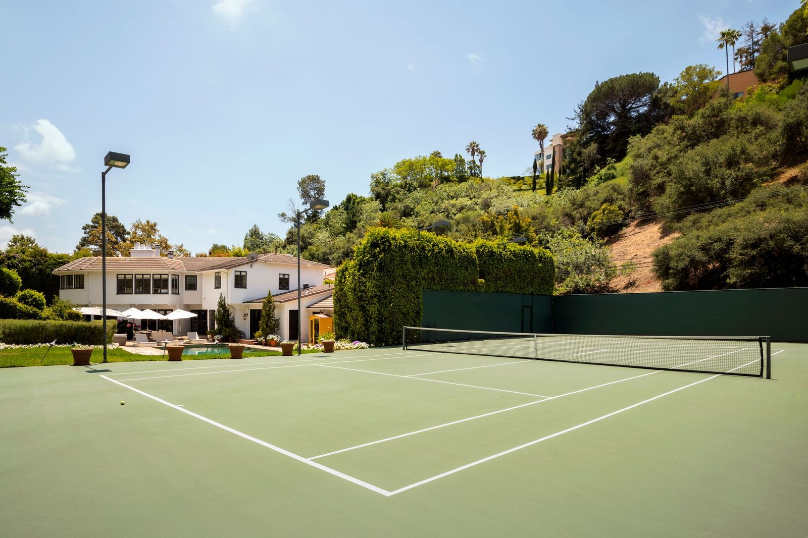 Set apart from the pool area, a full-size championship tennis court occupies its own secluded section of the grounds, bordered by tall hedges and the surrounding hillside.