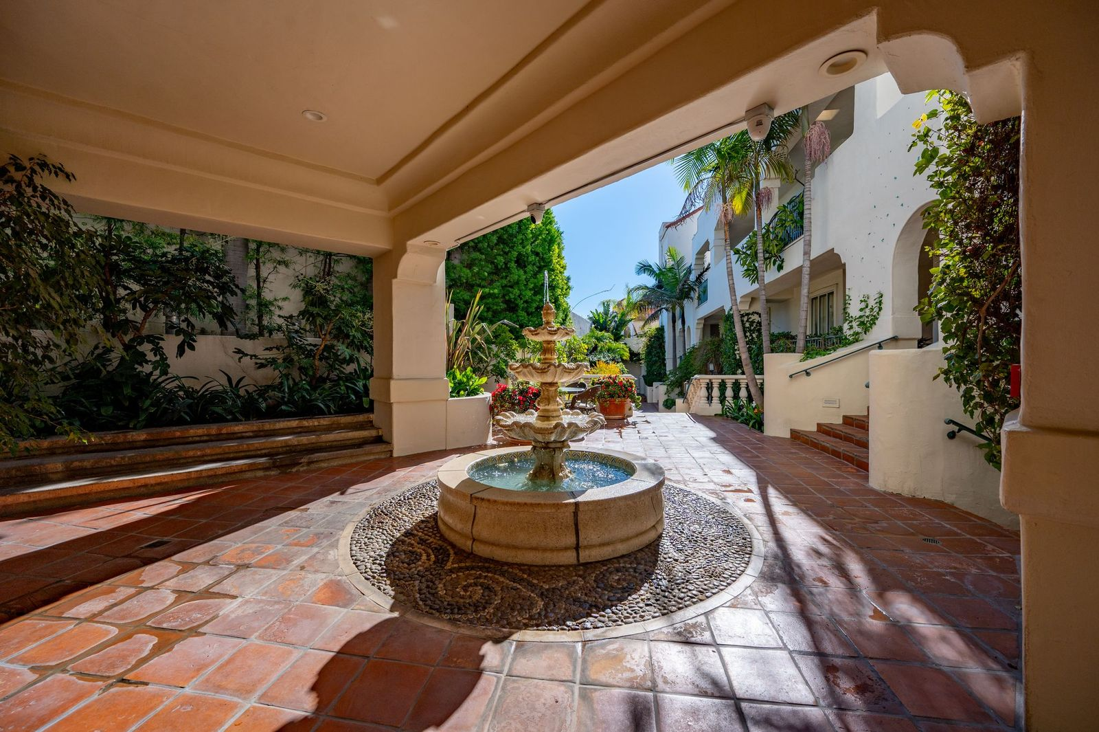 Spanish-inspired courtyards finished with terracotta tile, palm trees, flowering planters, and a central tiered fountain. 