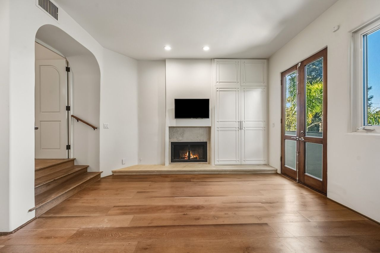 The room is centered around a contemporary fireplace alongside built-in storage, a mounted television, and French doors that bring in natural light while providing direct outdoor access.