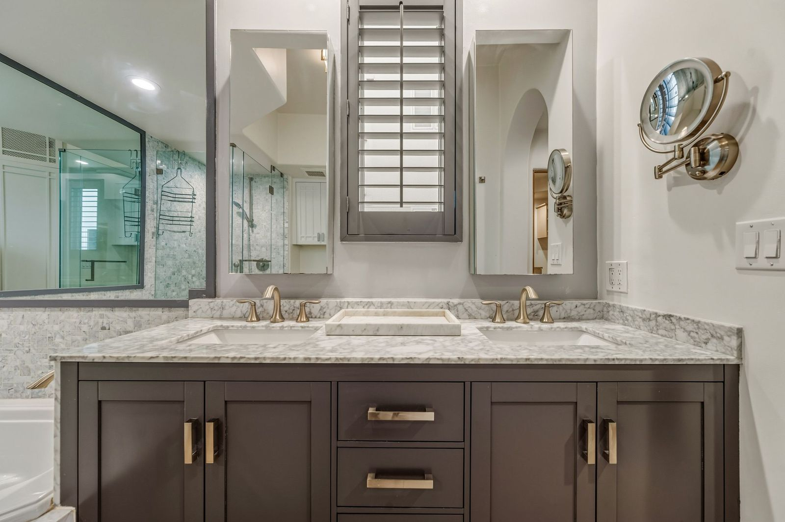 The spacious en-suite bathroom is finished with marble countertops, a dual-sink vanity, and walls lined in textured stone tile. 