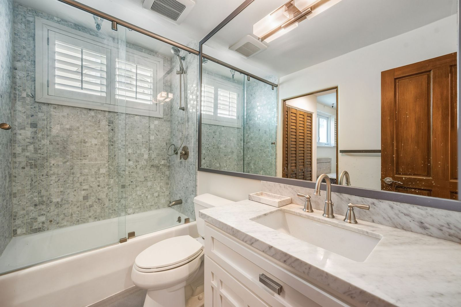 Bathroom is finished with marble countertops, a large vanity, and a tub-shower combination enclosed by a frameless glass partition. 