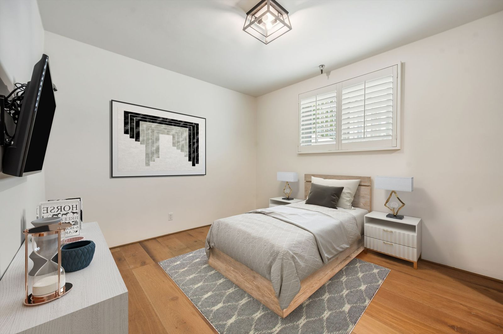 Guest room with wide-plank wood floors, soft neutral walls, and plantation shutters that filter in natural light. 