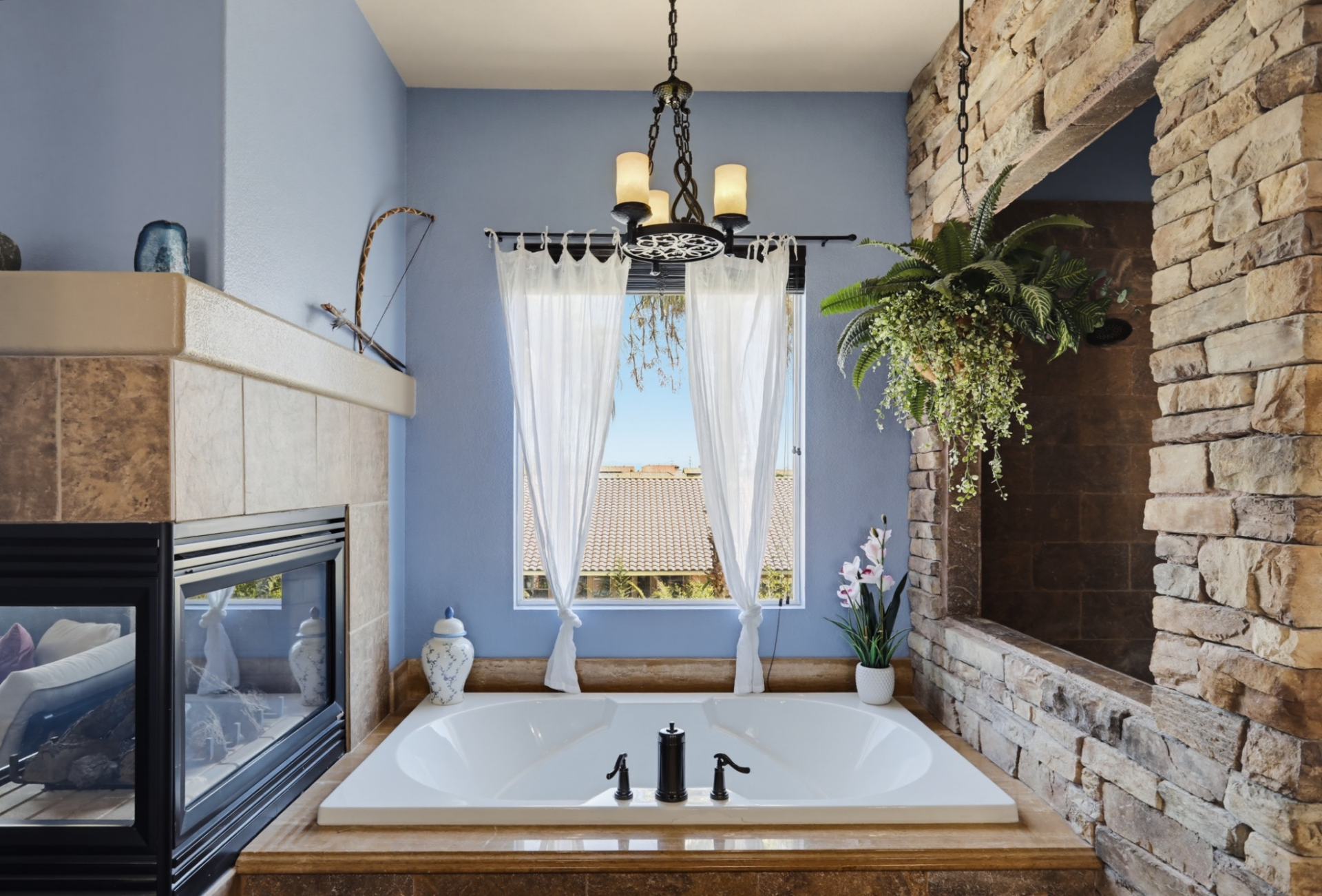 A soaking tub sits beneath tall windows, positioned between the double-sided fireplace and shower. 