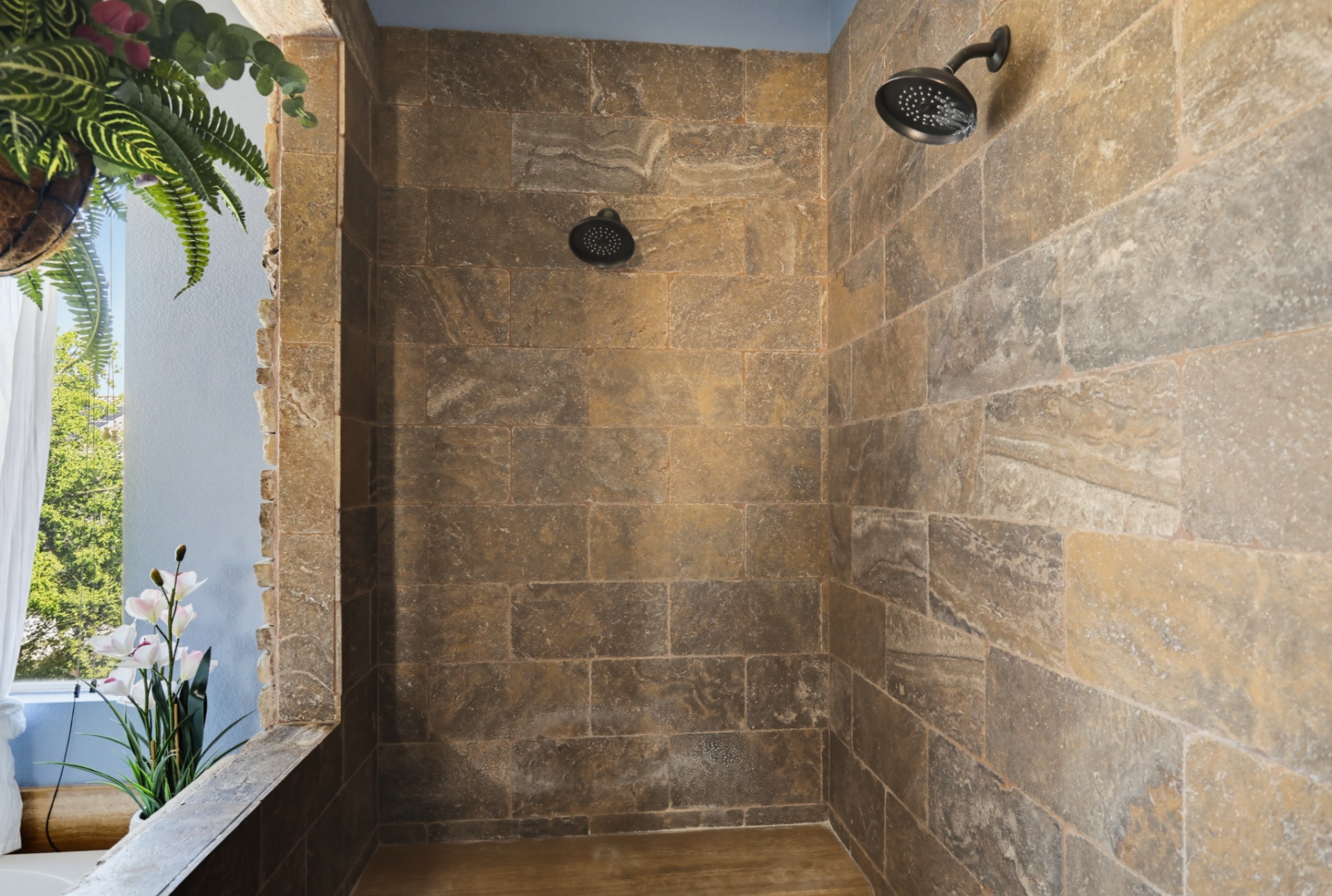 To the right of the tub, a large walk-in shower is finished with floor-to-ceiling stone tile and dual showerheads.