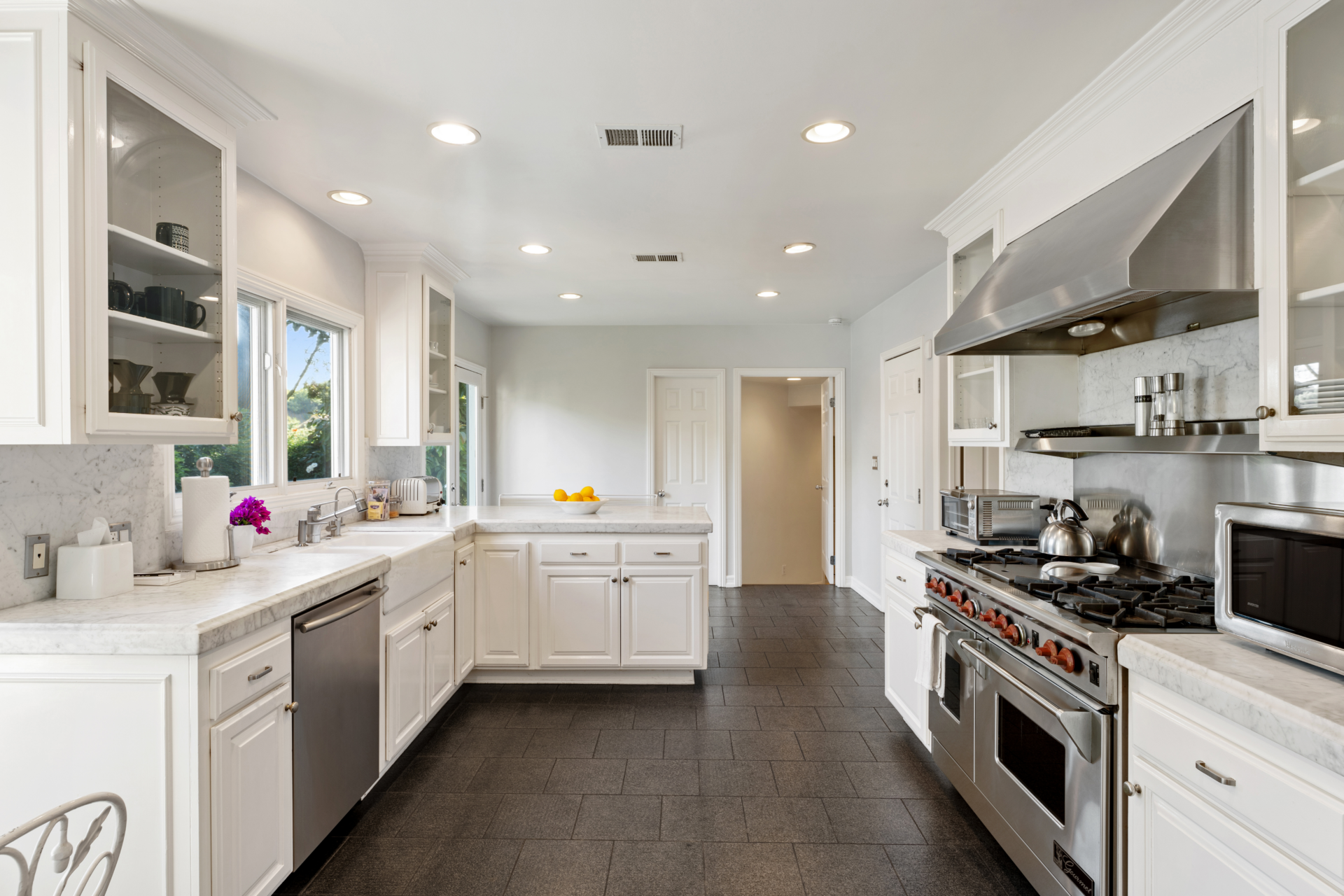 The kitchen features white shaker cabinetry, marble countertops, and stainless steel appliances anchored by a professional-grade gas range. 