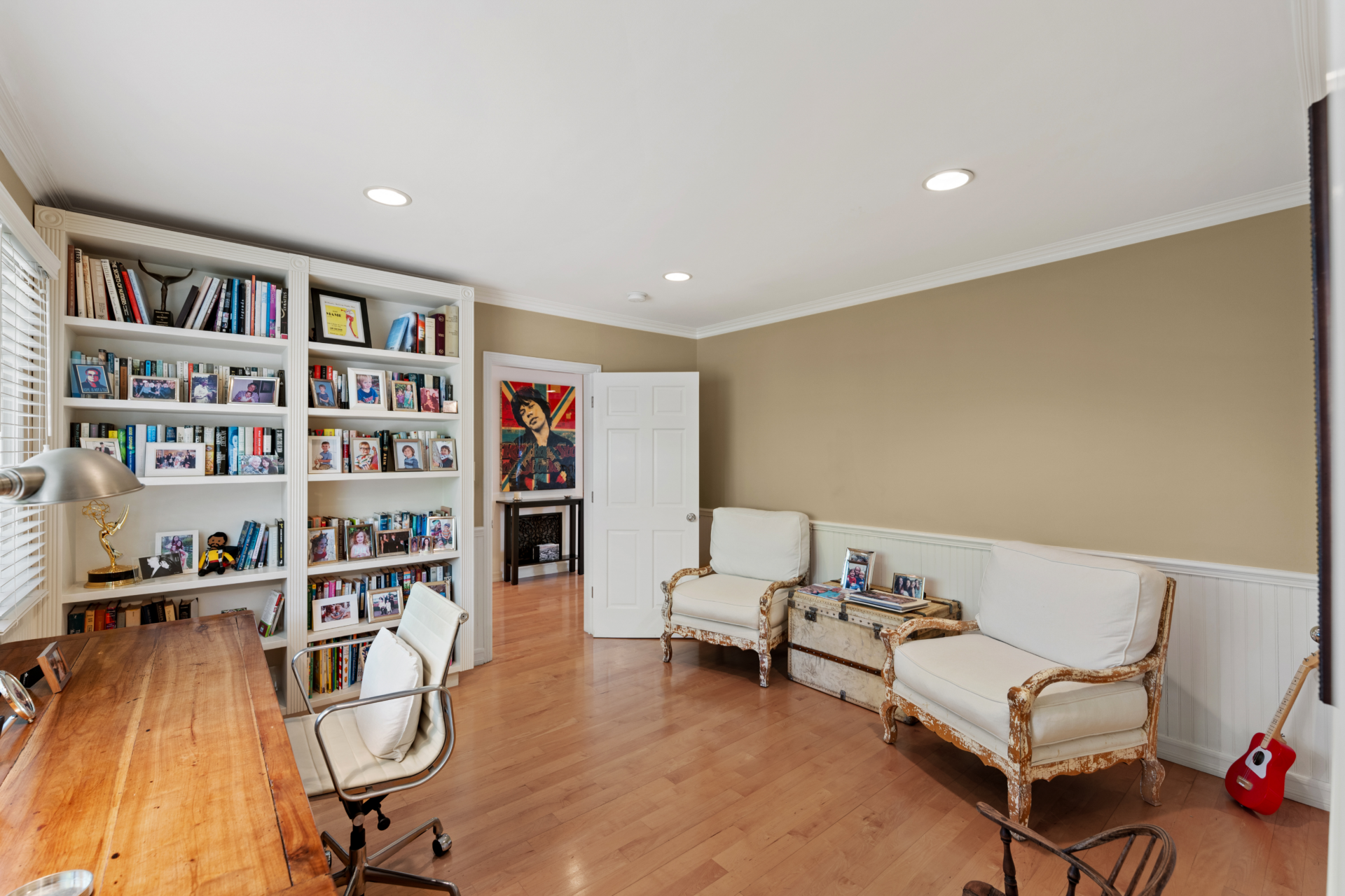 A bright study with custom built-in bookshelves, a long wood desk beneath the windows, and a pair of upholstered lounge chairs.