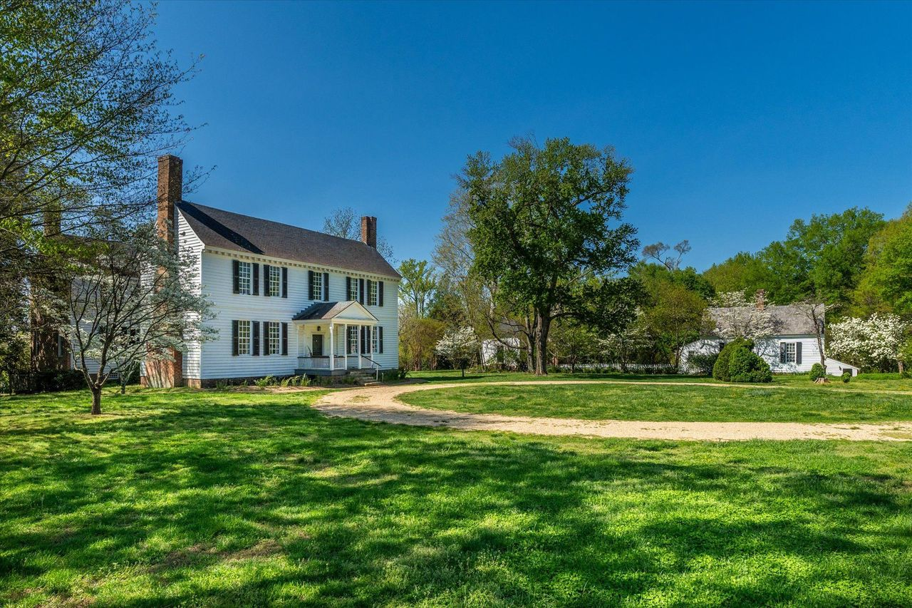 Towering trees frame the gravel drive, opening to a Georgian-style residence that stands at the center of the estate.