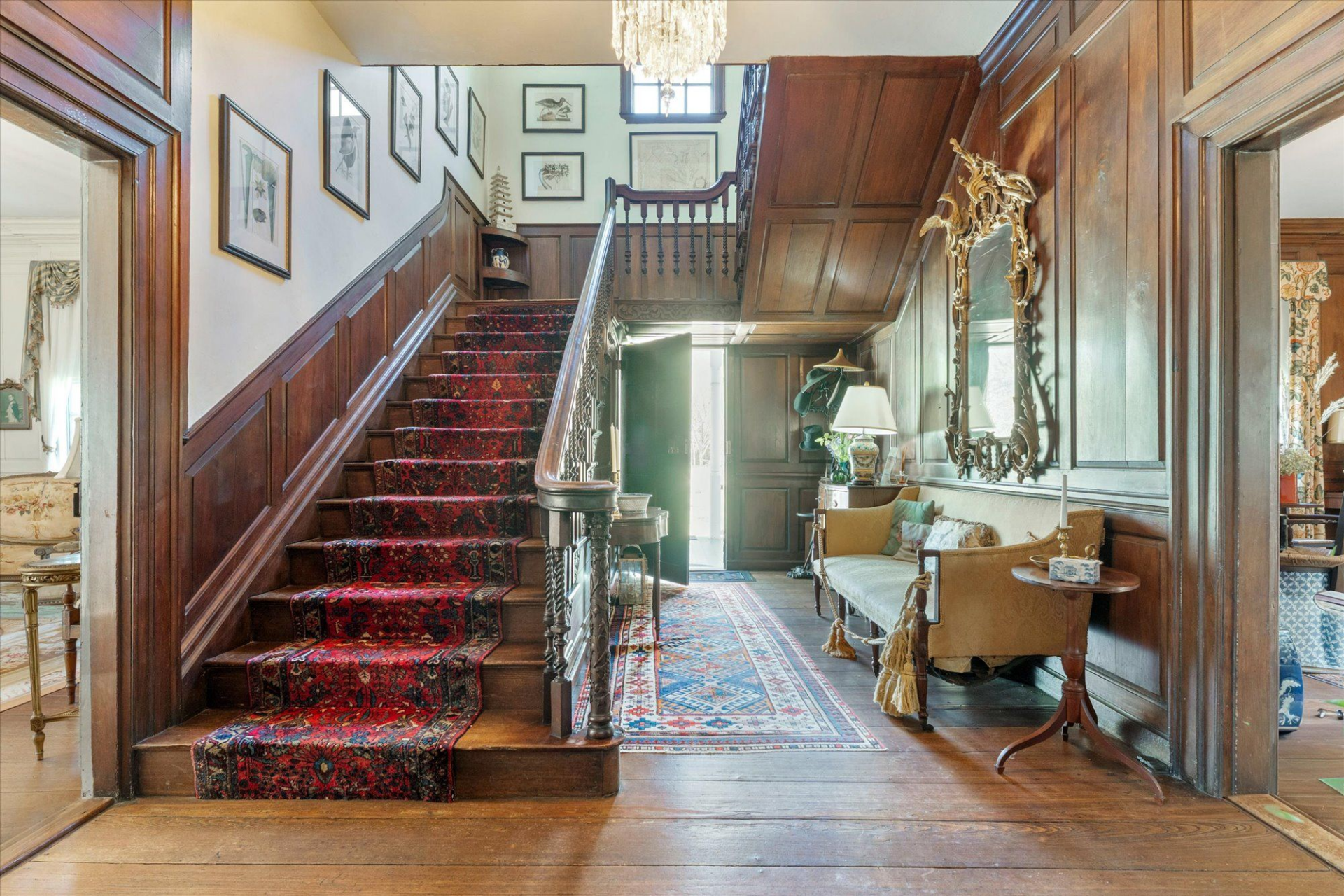 A grand central hall with rich wood paneling, wide-plank hardwood floors, and an original staircase.
